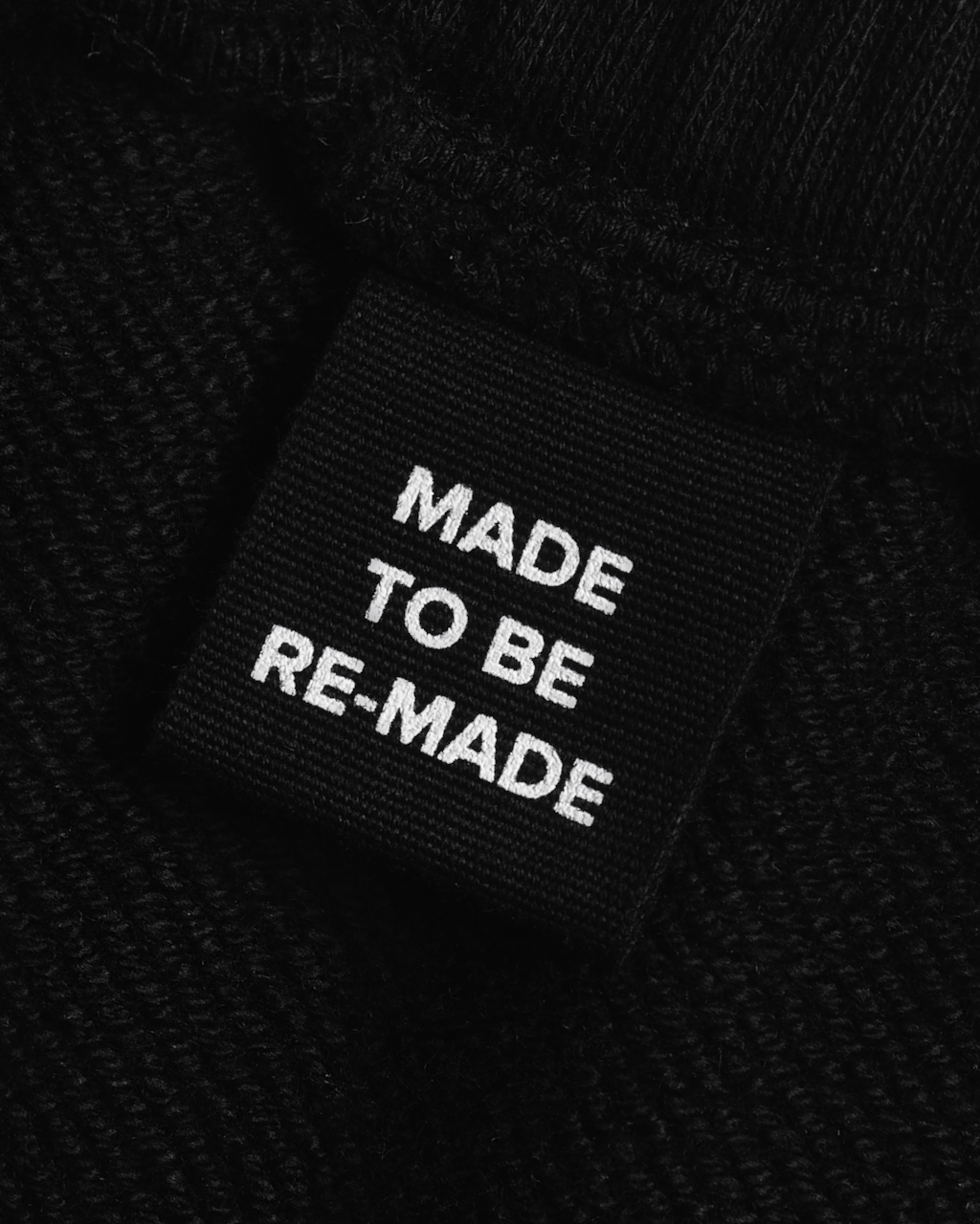A close up of a label tag in a pair of black, organic cotton joggers that says 'made to be re made'.