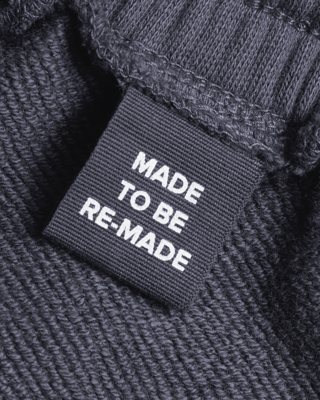A close up of a label tag in a pair of dark grey, organic cotton joggers that says 'made to be re made'.