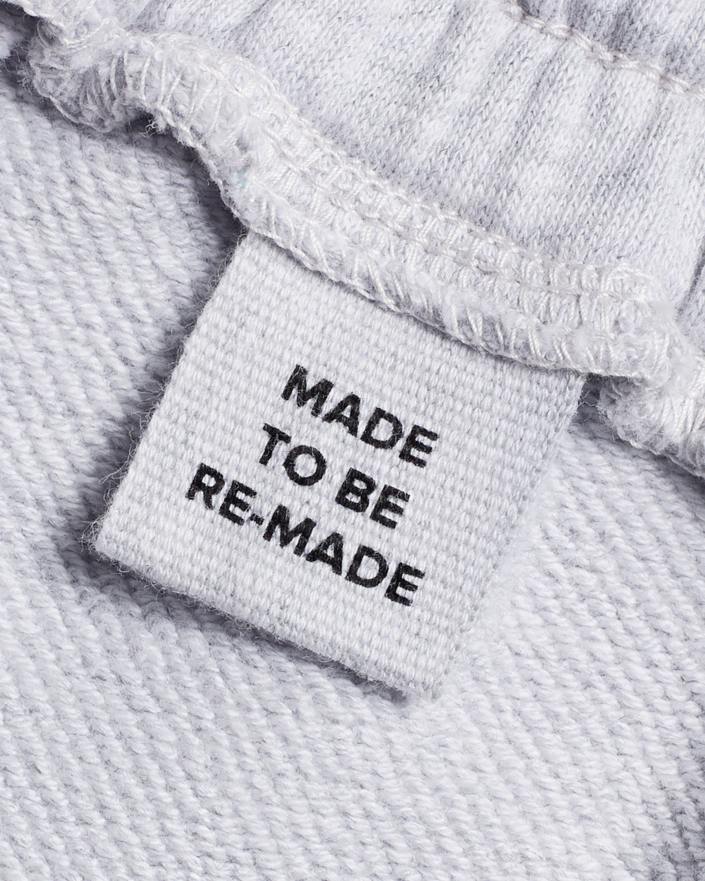 A close up of a label tag in a pair of grey, organic cotton joggers that says 'made to be re made'.