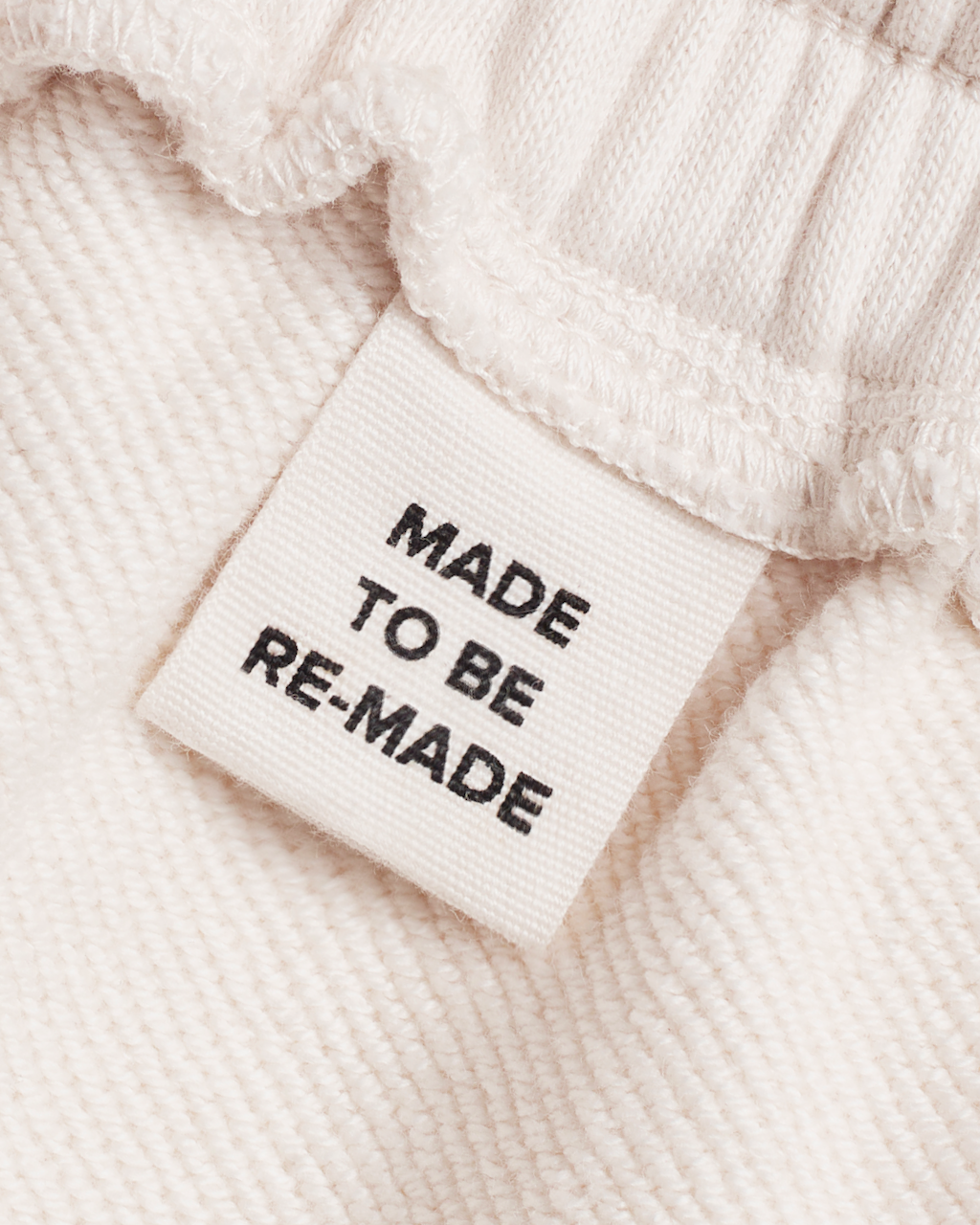 A close up of a label tag in a pair of natural coloured, organic cotton joggers that says 'made to be re made'.