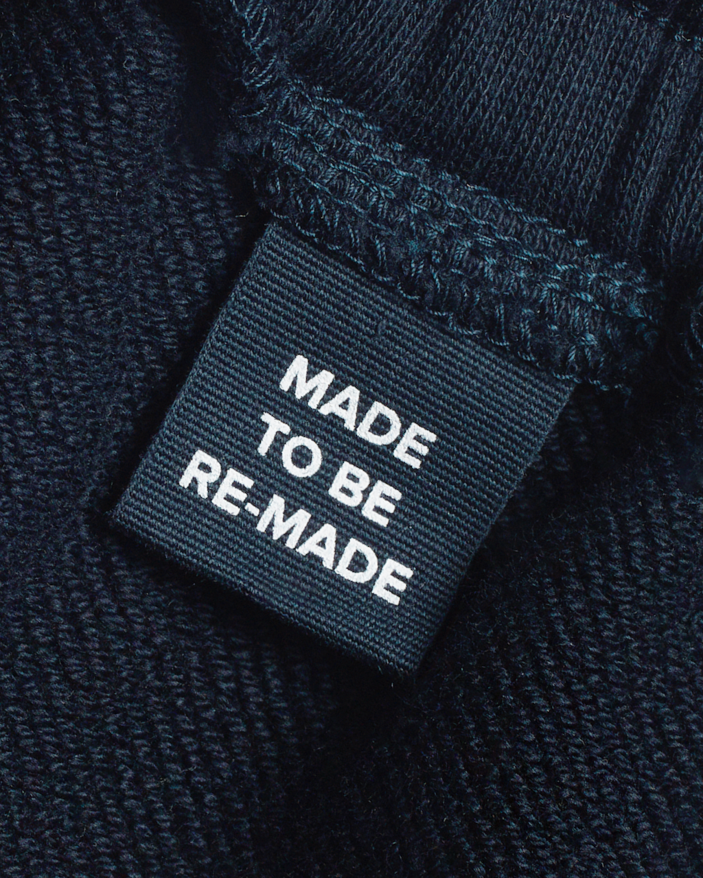 A close up of a label tag in a pair of navy, organic cotton joggers that says 'made to be re made'.