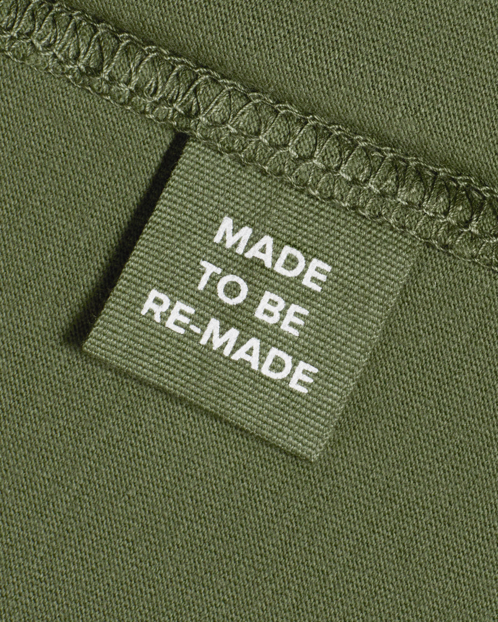 A close up of a label tag in a khaki green organic cotton t shirt that says 'made to be re made'.