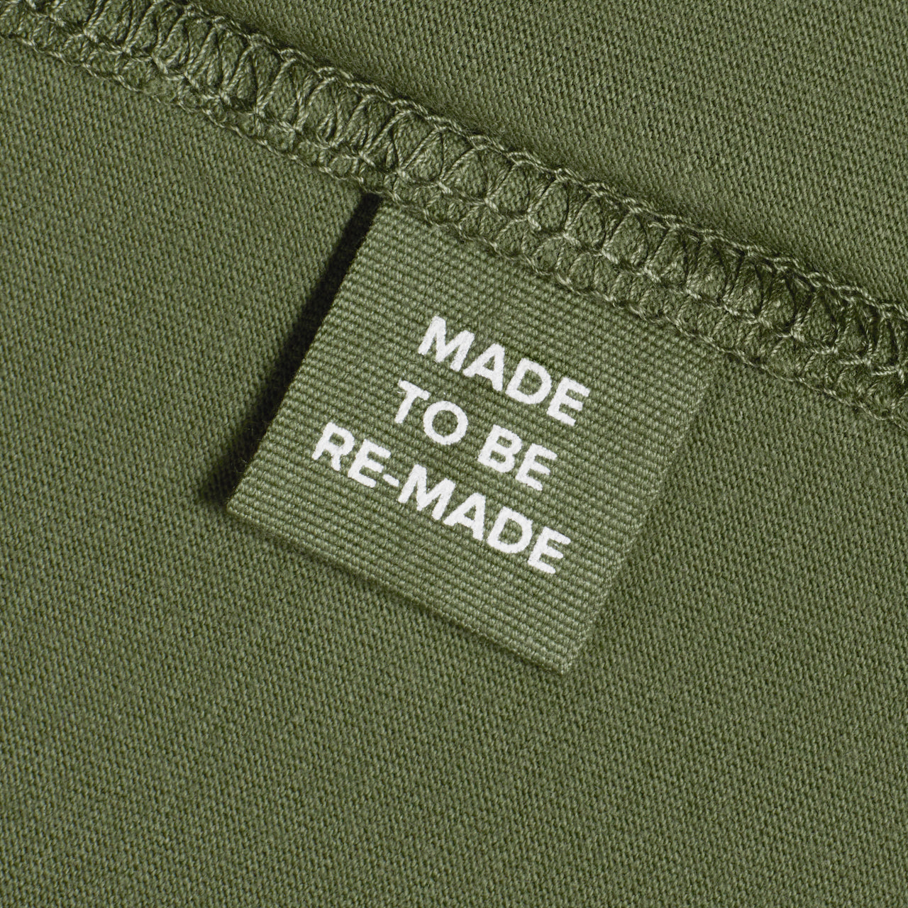 A close up of a label tag in a khaki green organic cotton t shirt that says 'made to be re made'.