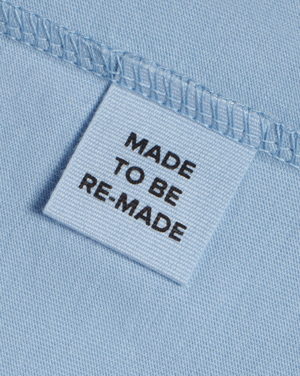 A close up of a label tag in a blue organic cotton t shirt that says 'made to be re made'.