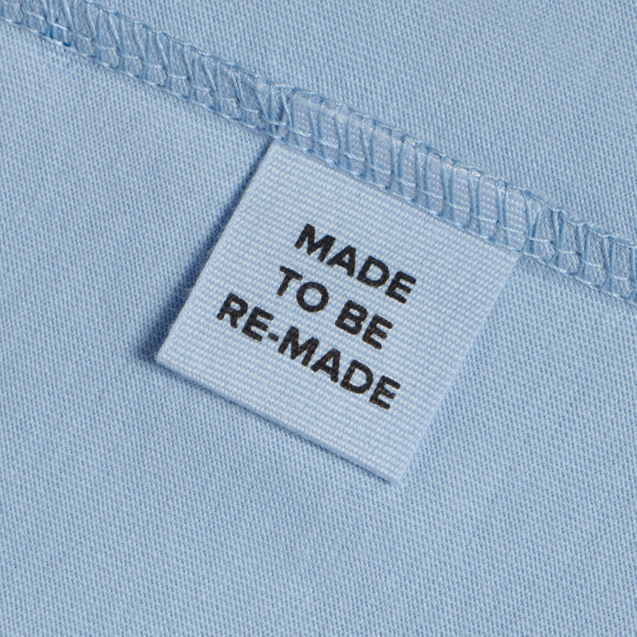 A close up of a label tag in a blue organic cotton t shirt that says 'made to be re made'.