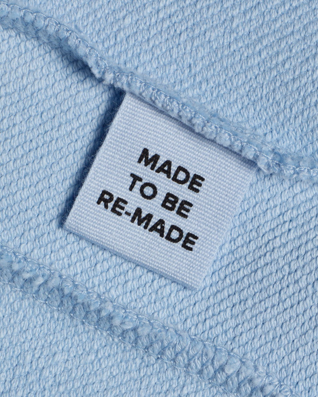 A close up of a label tag in a blue organic cotton sweatshirt that says 'made to be re made'.
