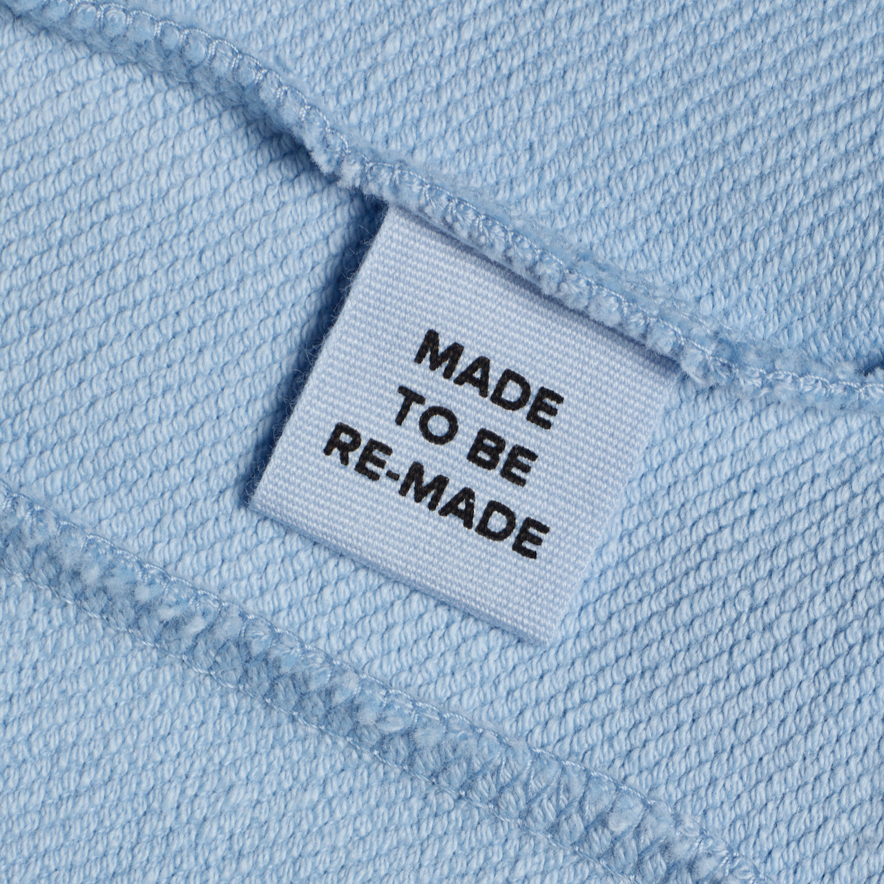 A close up of a label tag in a blue organic cotton sweatshirt that says 'made to be re made'.