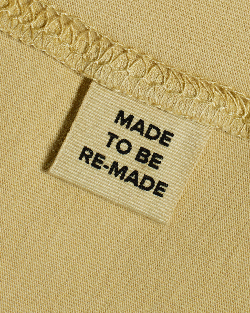 A close up of a label tag in a light khaki organic cotton t shirt that says 'made to be re made'.