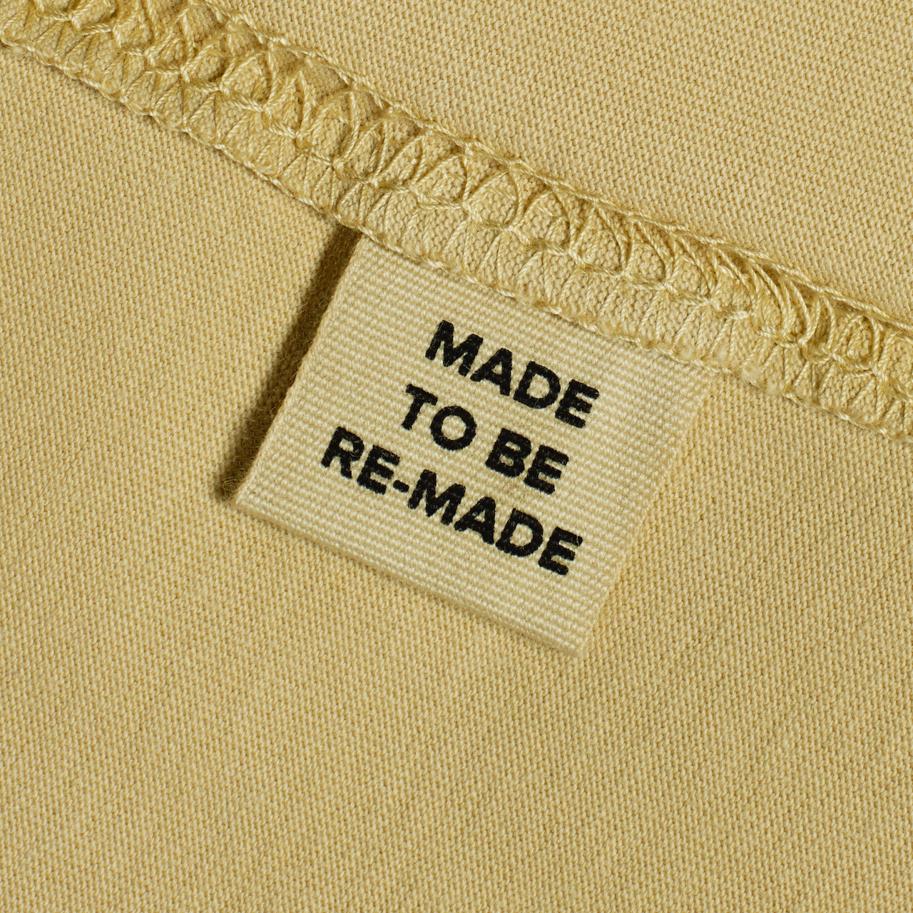 A close up of a label tag in a light khaki organic cotton t shirt that says 'made to be re made'.