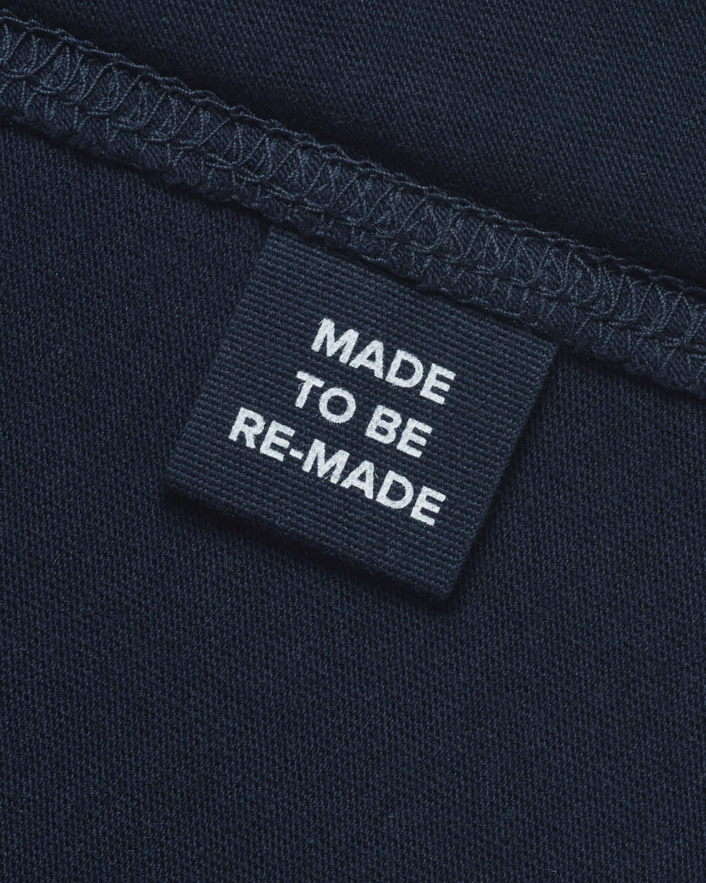 A close up of a label tag in a navy organic cotton t shirt that says 'made to be re made'.
