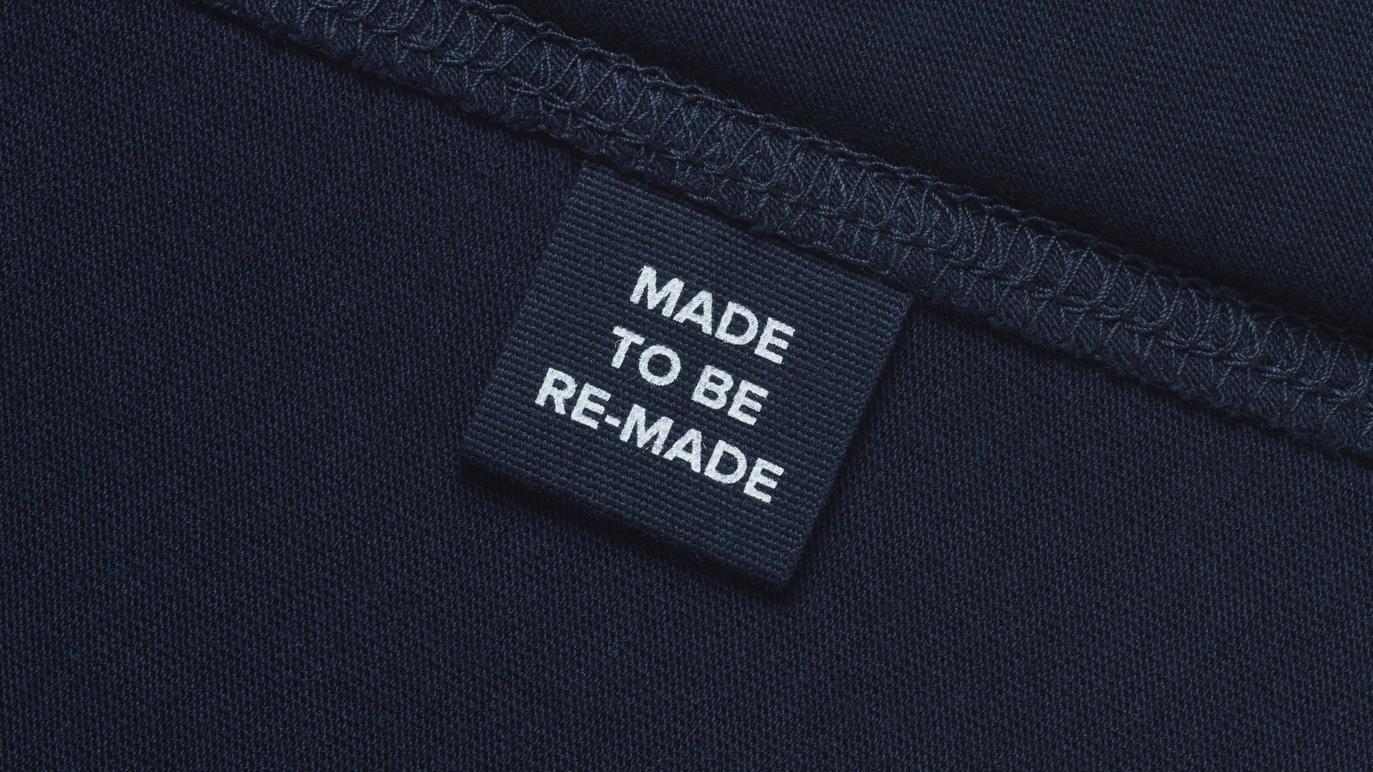A close up of a label tag in a navy organic cotton t shirt that says 'made to be re made'.