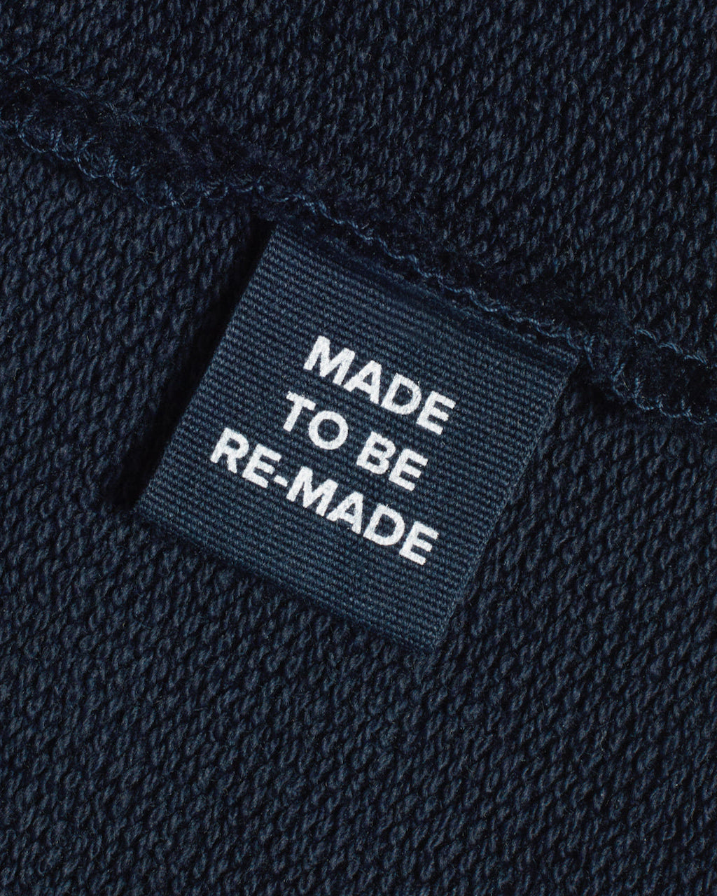 A close up of a label tag in a navy organic cotton sweatshirt that says 'made to be re made'.