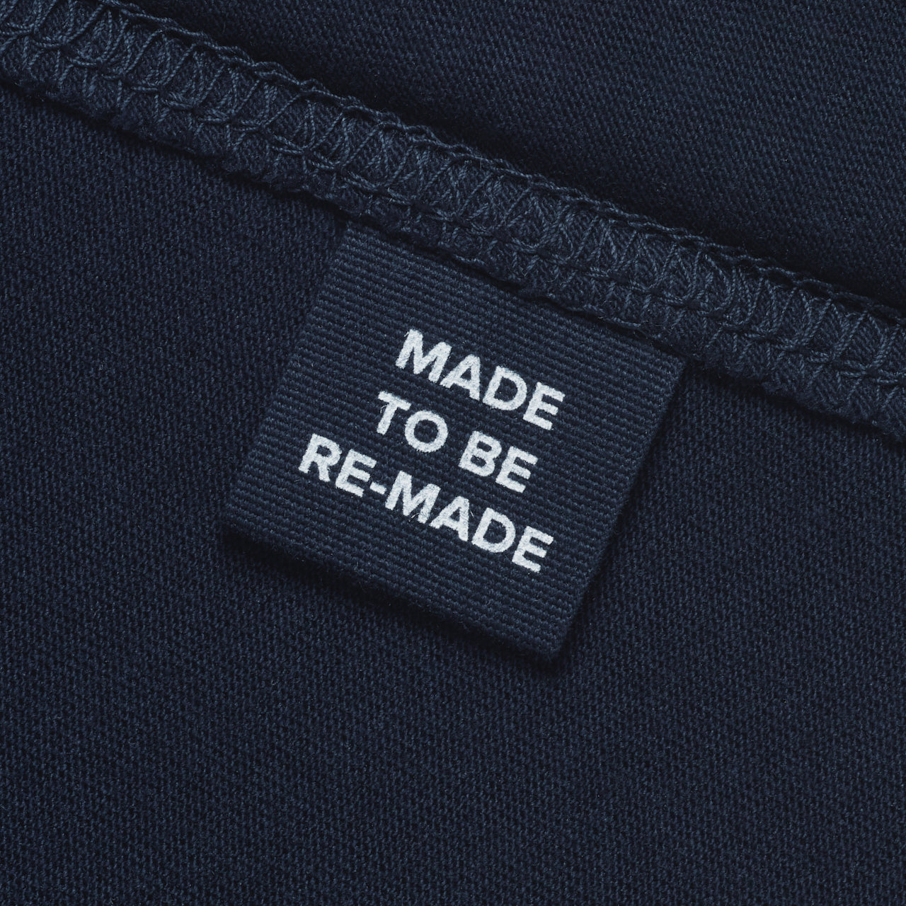 A close up of a label tag in a navy organic cotton t shirt that says 'made to be re made'.