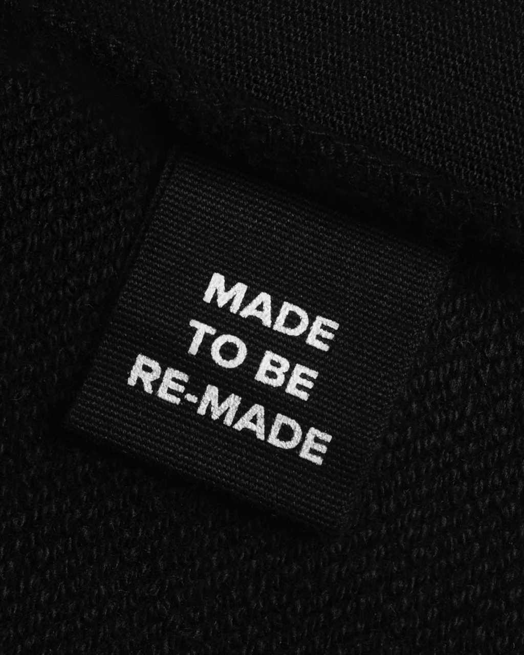 A close up of a label tag in a black, organic cotton overshirt that says 'made to be re made'.