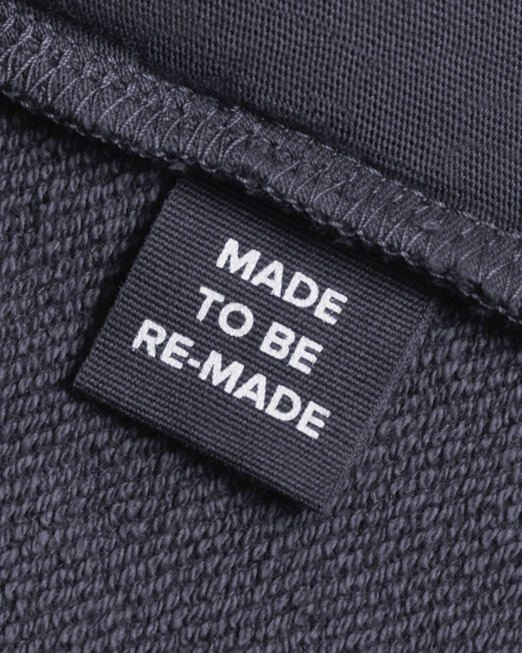 A close up of a label tag in a dark grey, organic cotton overshirt that says 'made to be re made'.