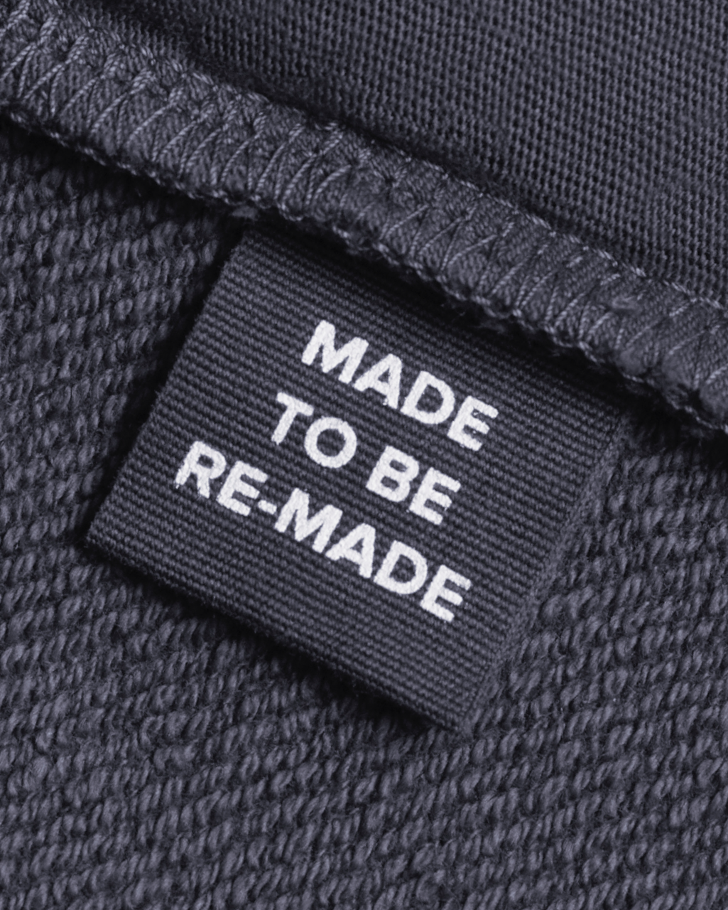 A close up of a label tag in a dark grey, organic cotton overshirt that says 'made to be re made'.
