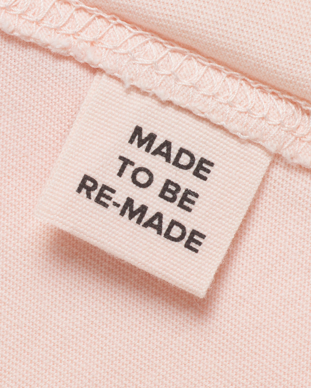 A close up of a label tag in a pink organic cotton t shirt that says 'made to be re made'.