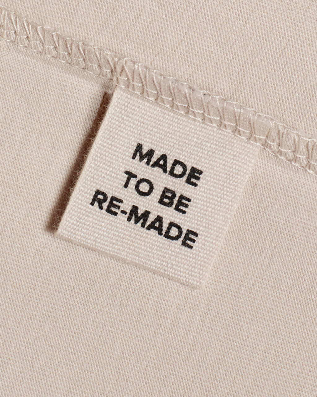 A close up of a label tag in an ecru organic cotton t shirt that says 'made to be re made'.