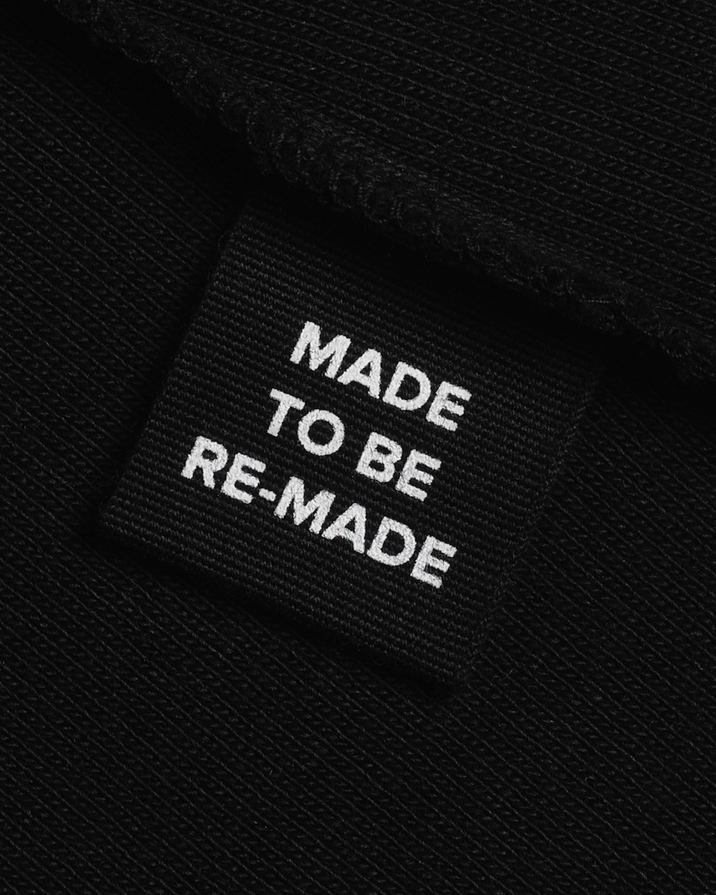 A close up of a label tag in a black, organic cotton tank top that says 'made to be re made'.