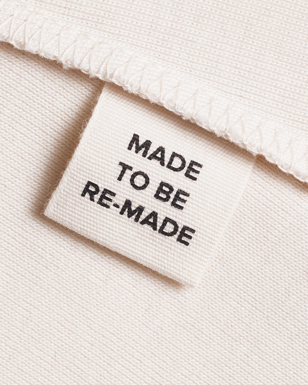 A close up of a label tag in a natural coloured, organic cotton tank top that says 'made to be re made'.