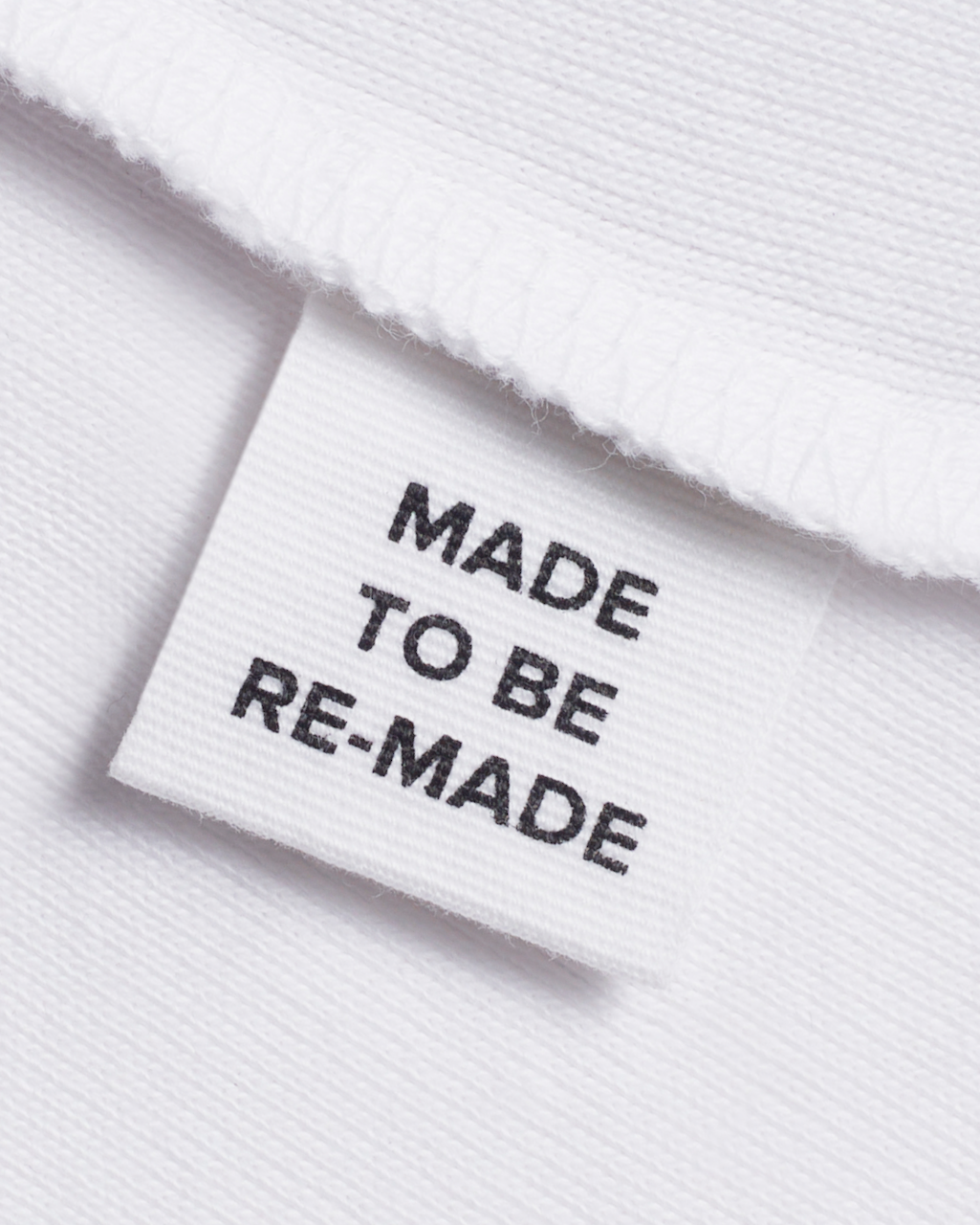 A close up of a label tag in a white, organic cotton tank top that says 'made to be re made'.