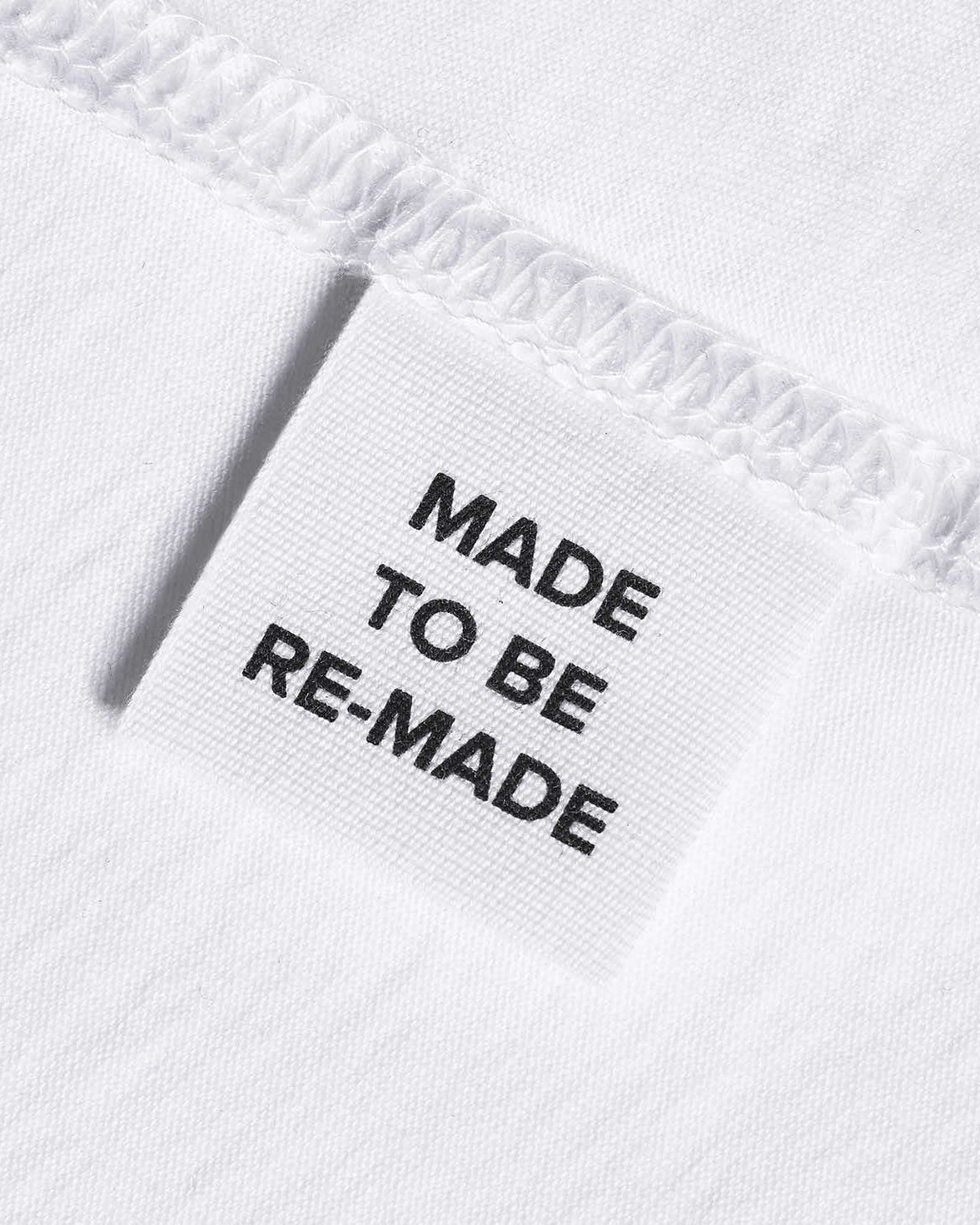 A close up of a label tag in a white organic cotton t shirt that says 'made to be re made'.