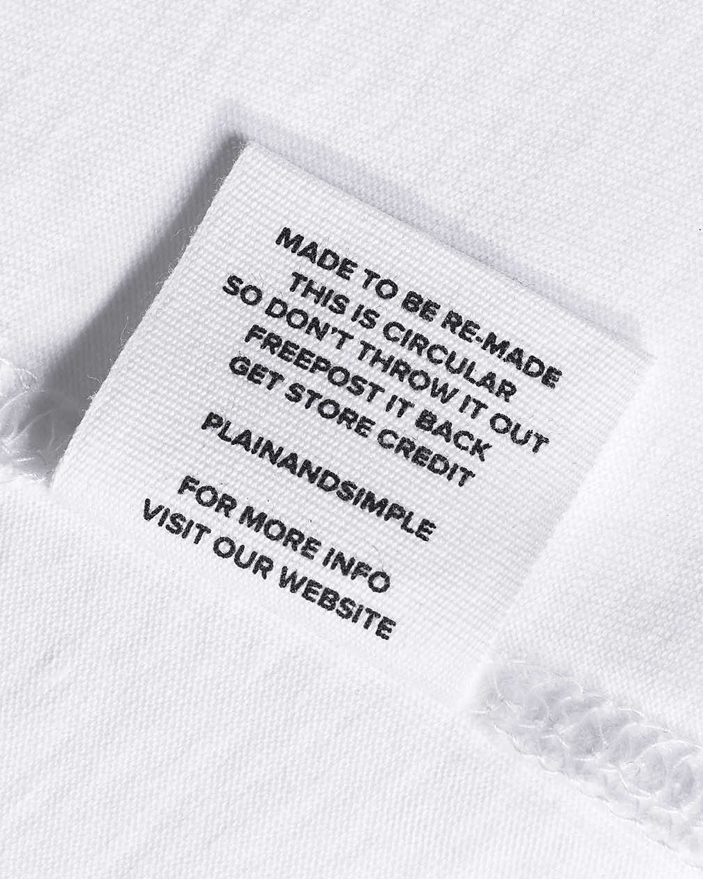 A close-up of a label in a white organic cotton t shirt, saying 'made to be re made this is circular so don't throw it out freepost it back get store credit'