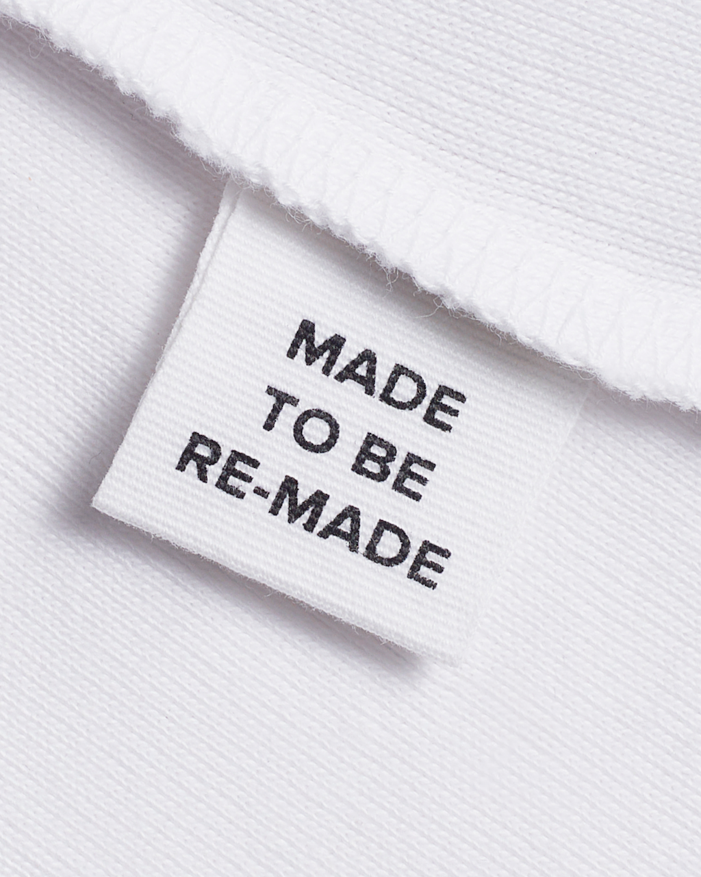 A close up of a label tag in a white, organic cotton tank top that says 'made to be re made'.