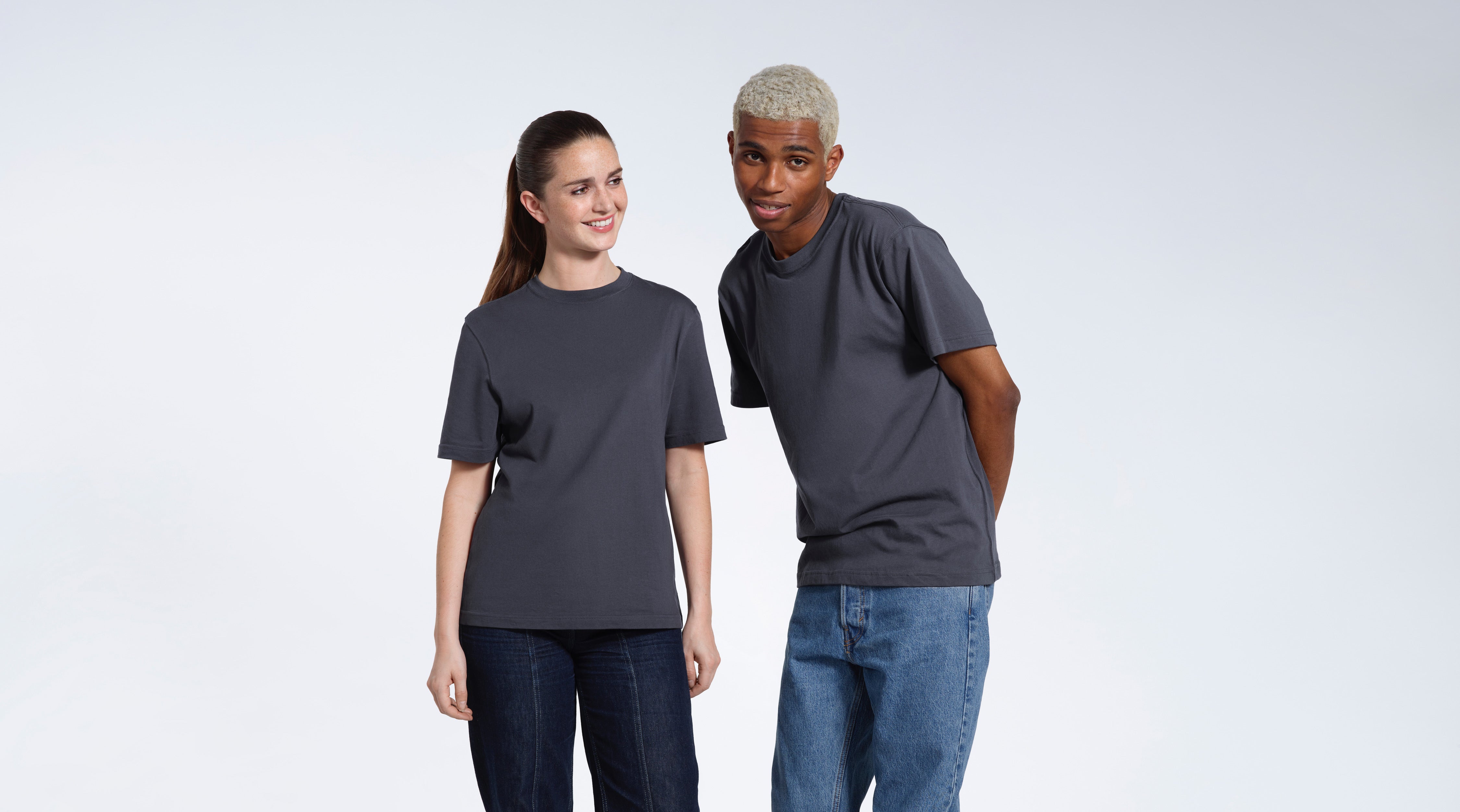 A man and woman smiling, wearing matching dark grey short sleeve organic cotton t shirts.