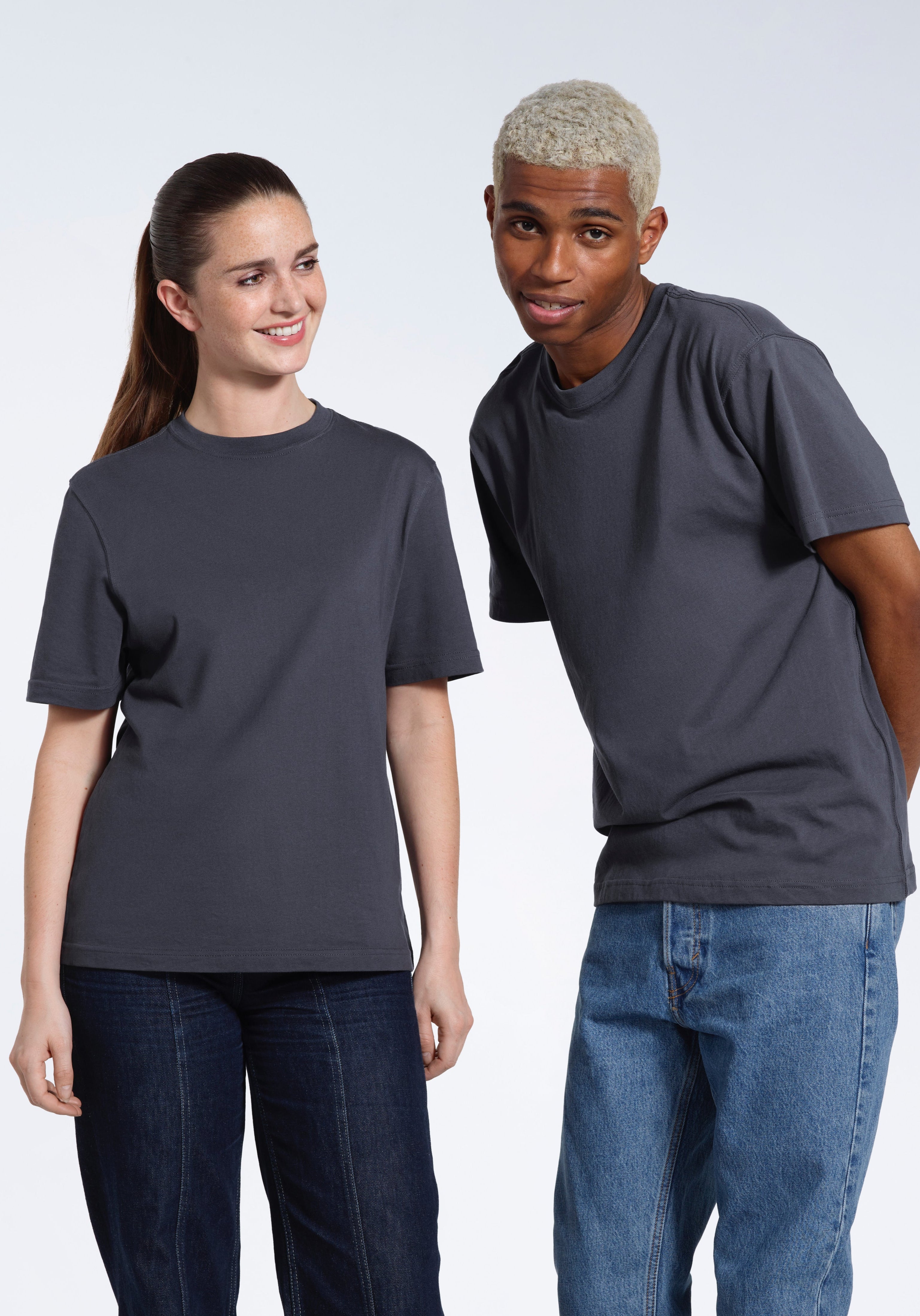 A man and woman smiling, wearing matching dark grey short sleeve organic cotton t shirts.
