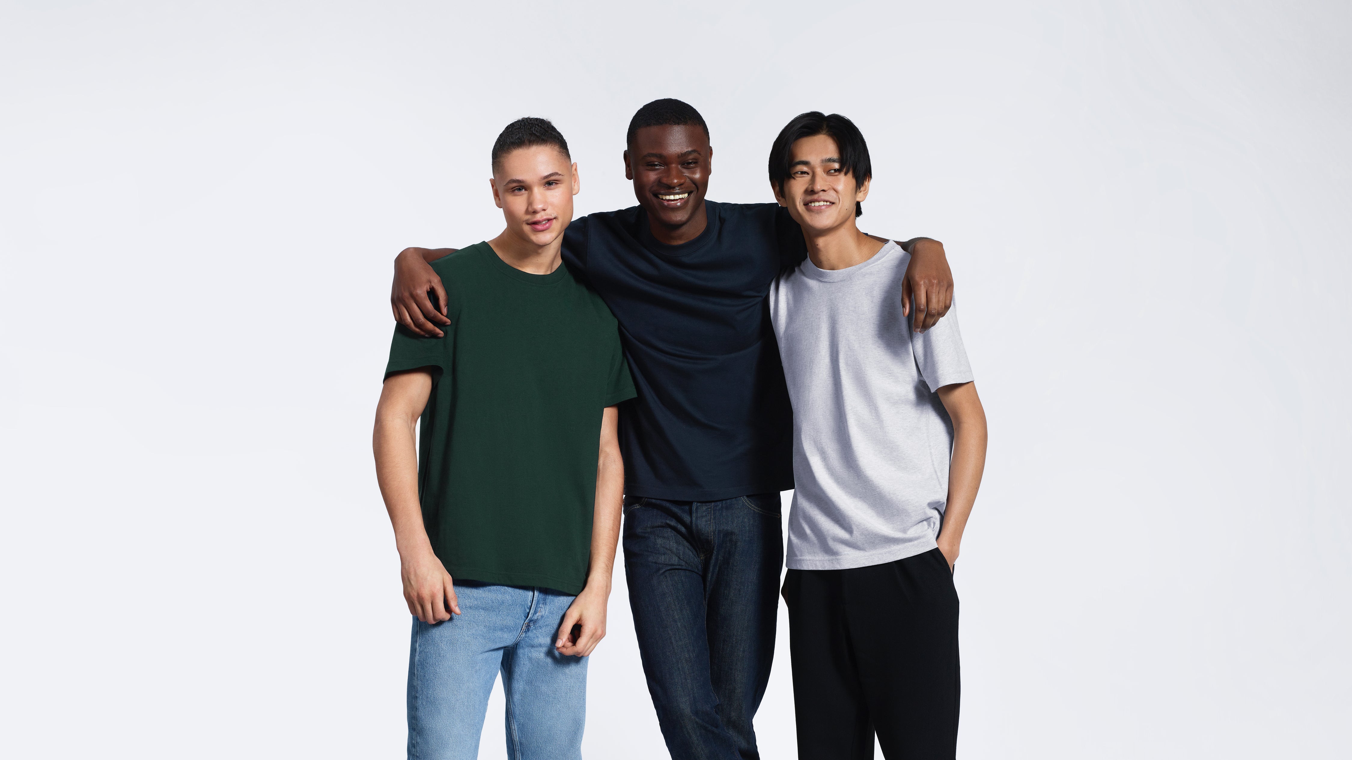 Three men smiling with their arms round eachother, modelling plain green, navy and grey organic cotton t shirts.