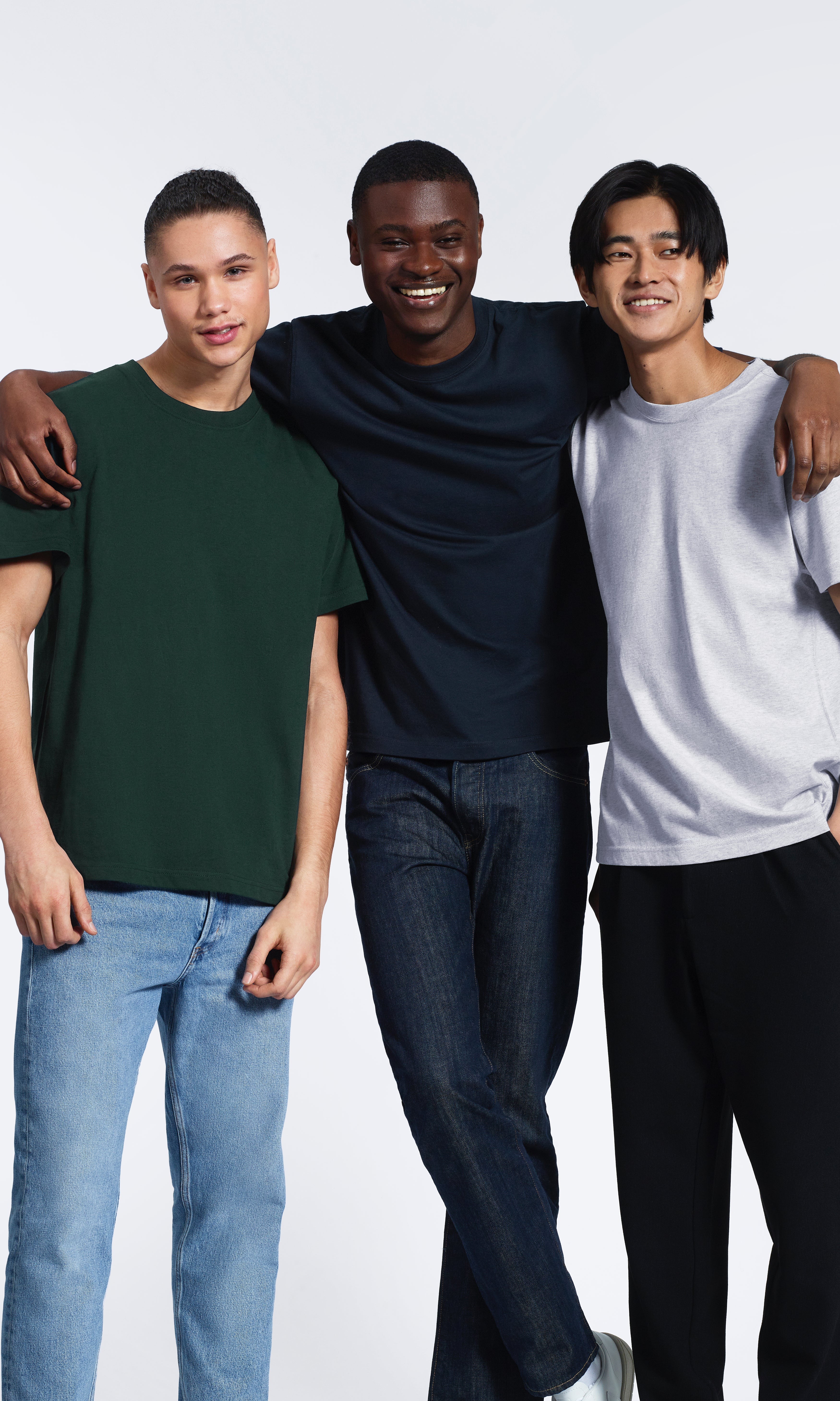 Three men smiling with their arms round eachother, modelling plain green, navy and grey organic cotton t shirts.
