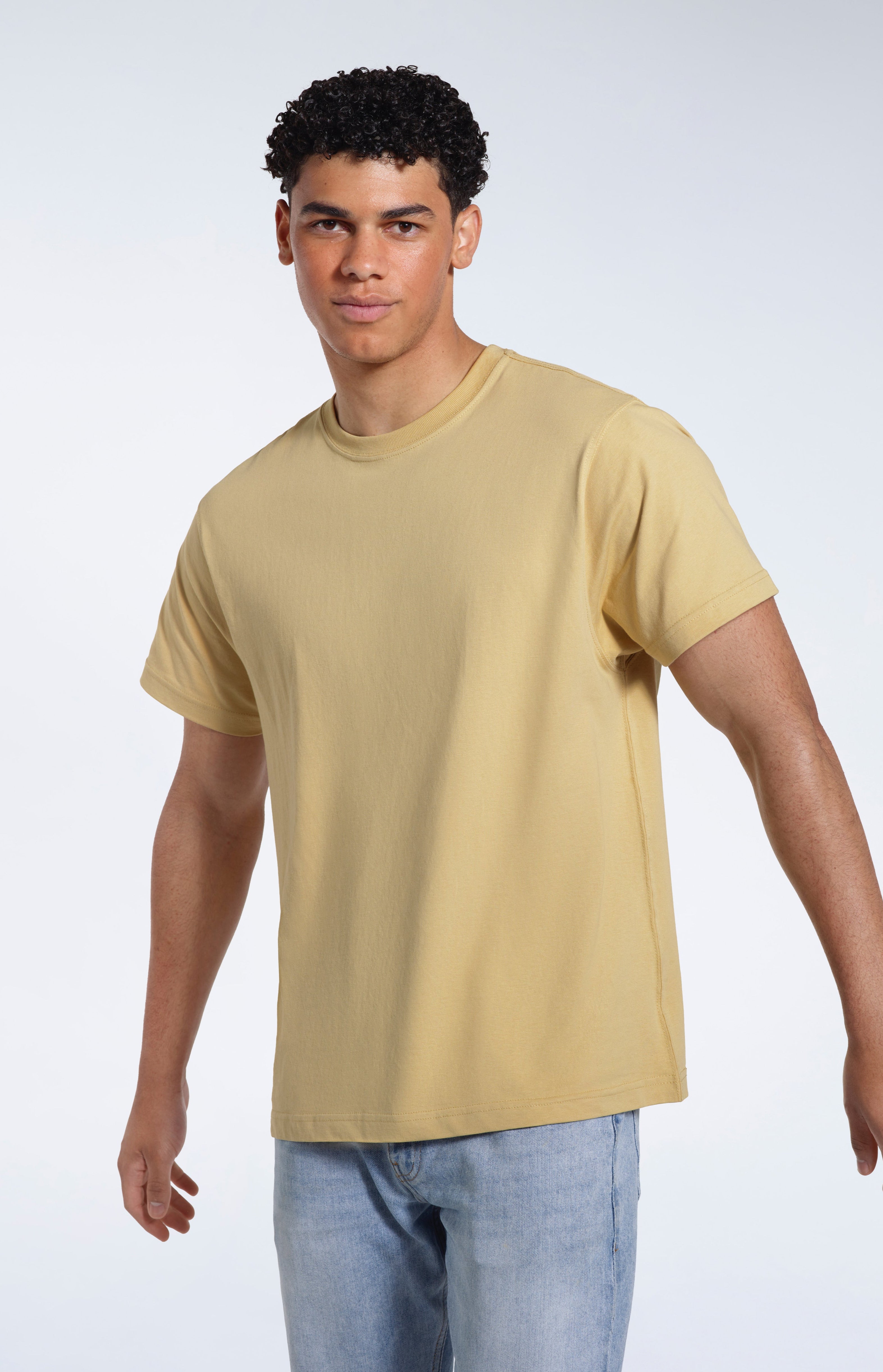 A man looking into the camera, modelling a light khaki organic cotton t shirt.