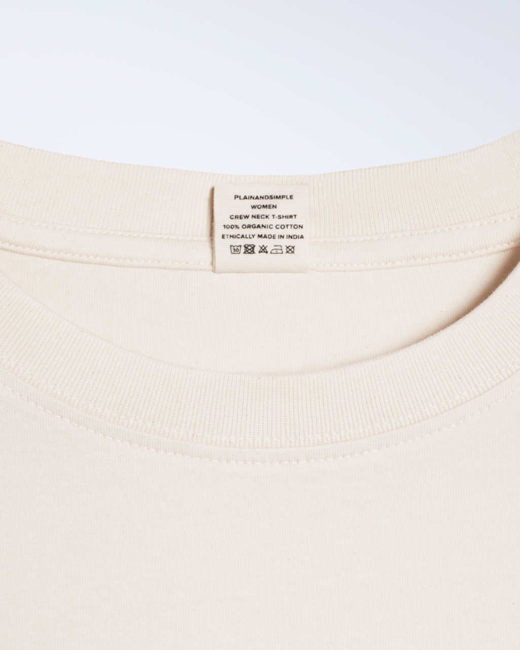 A close up of the neck label in a natural coloured, crew neck, organic cotton t shirt.