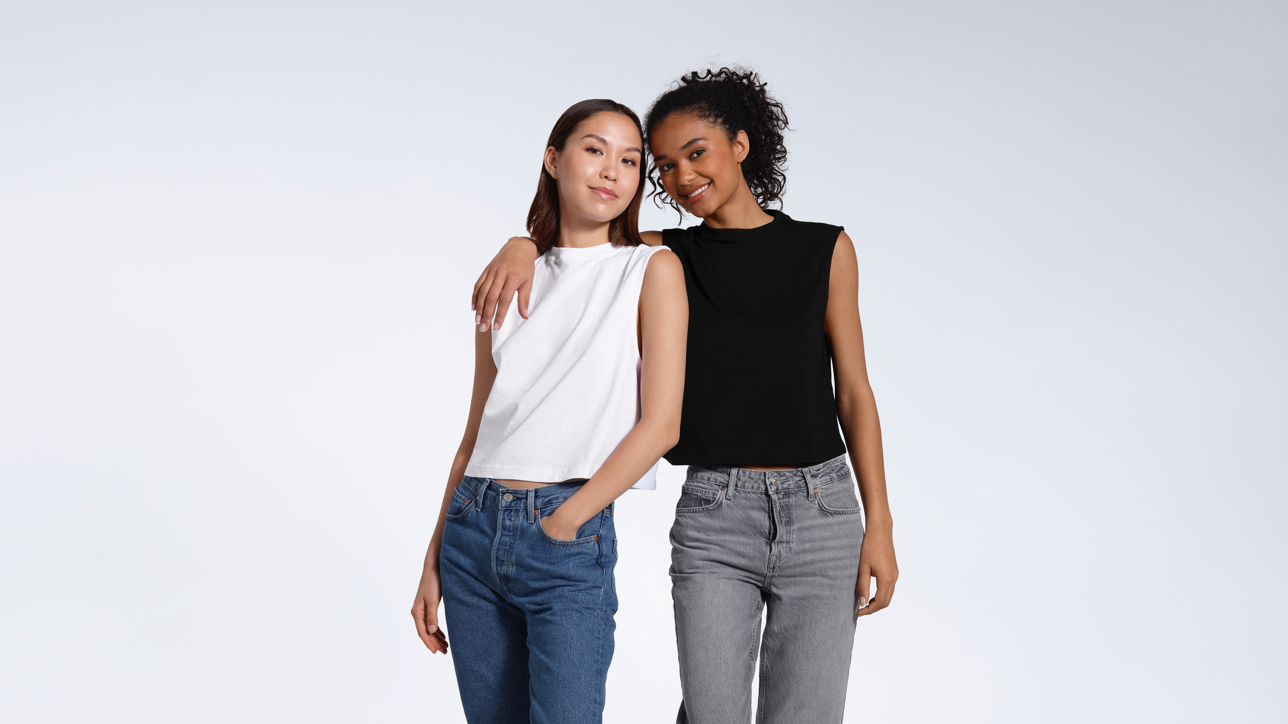 Two women smiling into the camera, modelling plain black and white, organic cotton, crew neck tank tops.