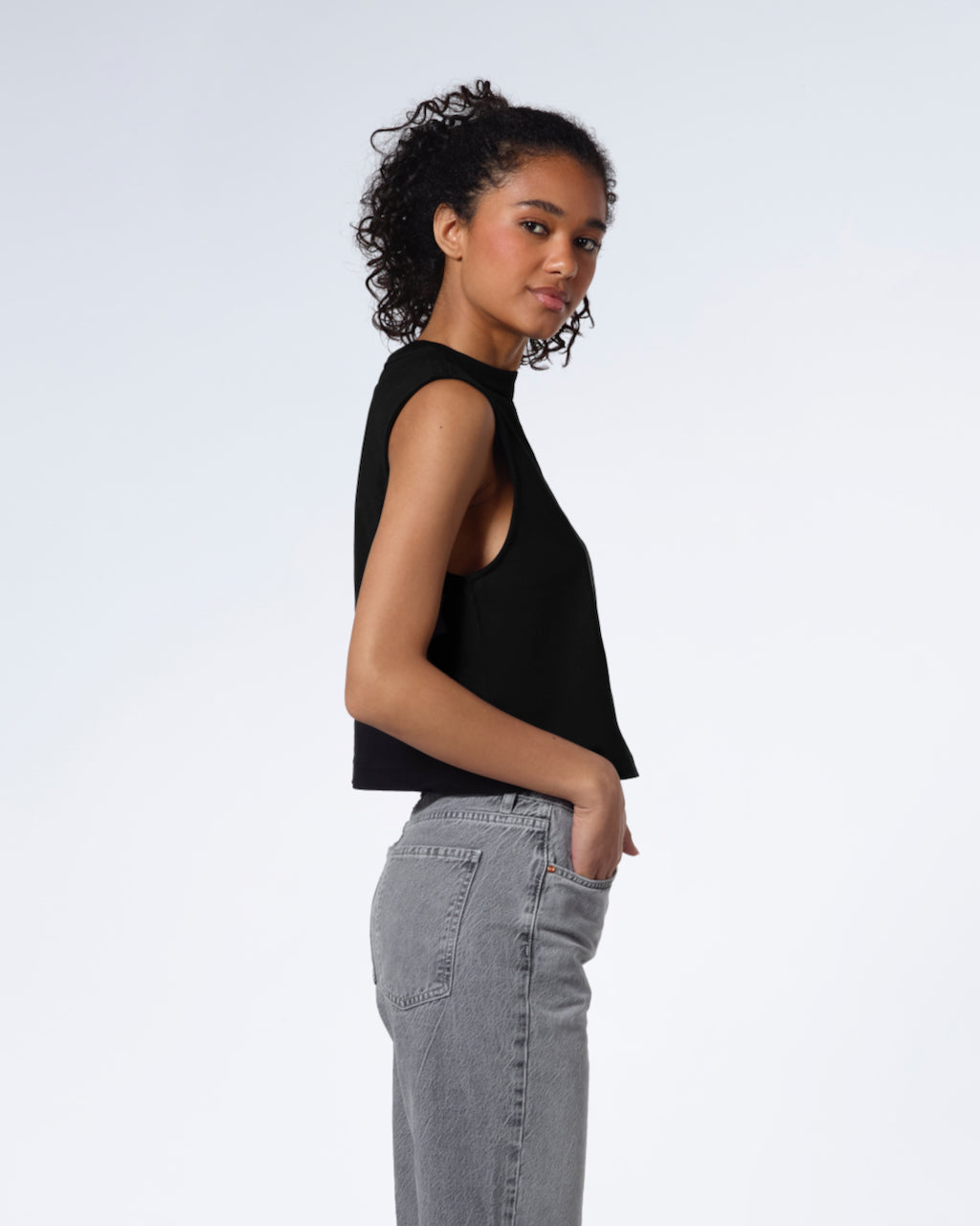 A woman facing side on and looking at the camera, modelling a plain black sleeveless organic cotton tank top.