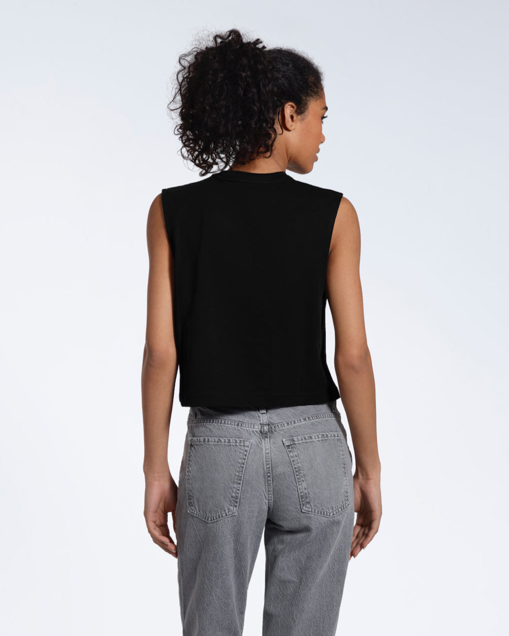A woman with her back to the camera, modelling a plain black sleeveless organic cotton tank top.