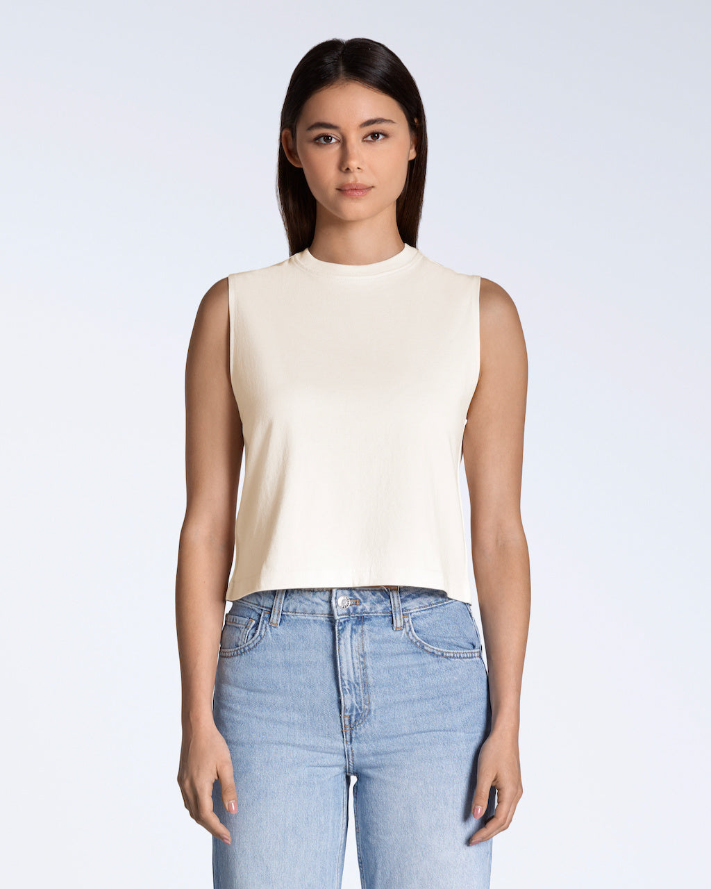 A woman facing front on looking into the camera, modelling a plain natural coloured, organic cotton, crew neck tank top.