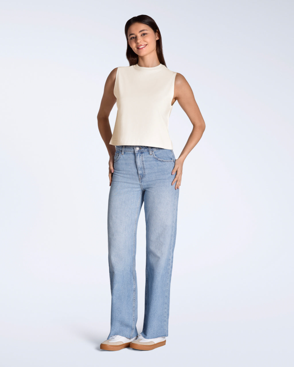 A full body photo of a woman smiling into the camera, modelling plain natural coloured, organic cotton crew neck tank top.