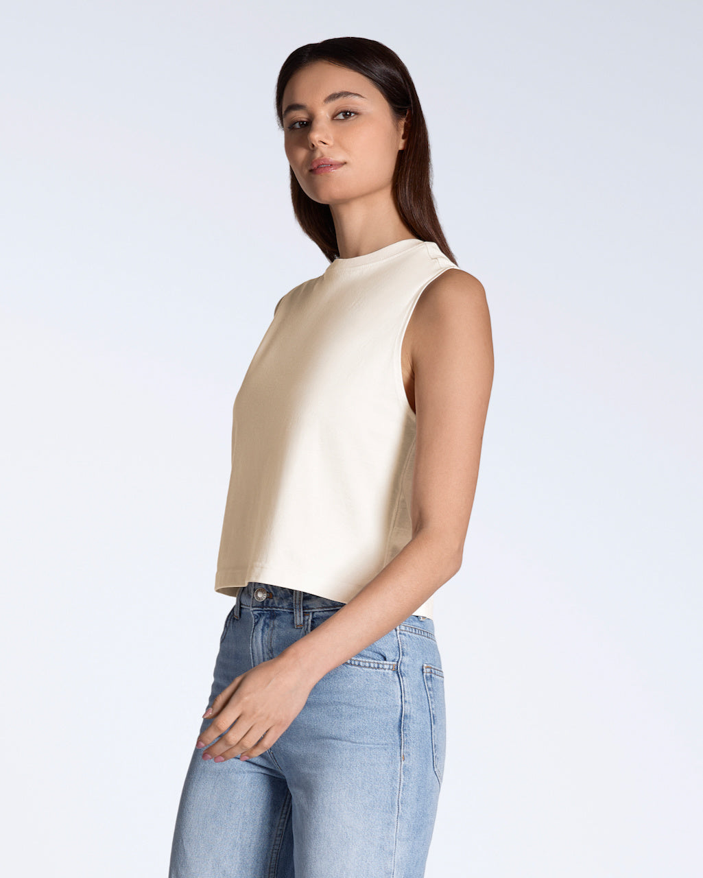 A woman looking into the camera, modelling a plain natural coloured, organic cotton, crew neck tank top.