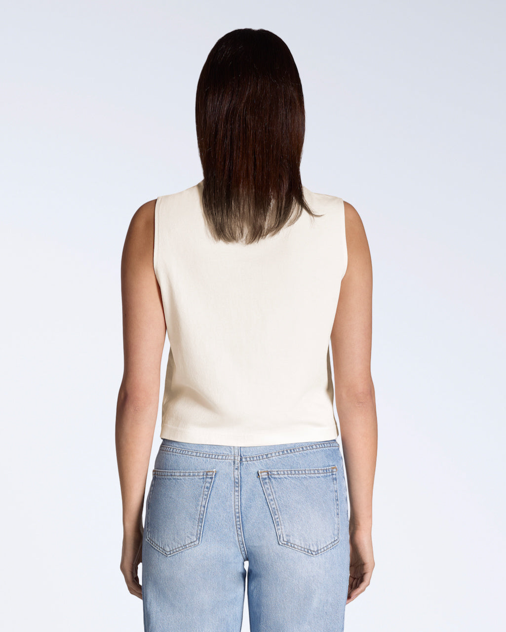 A woman facing away from the camera, modelling a plain natural coloured, organic cotton, crew neck tank top.