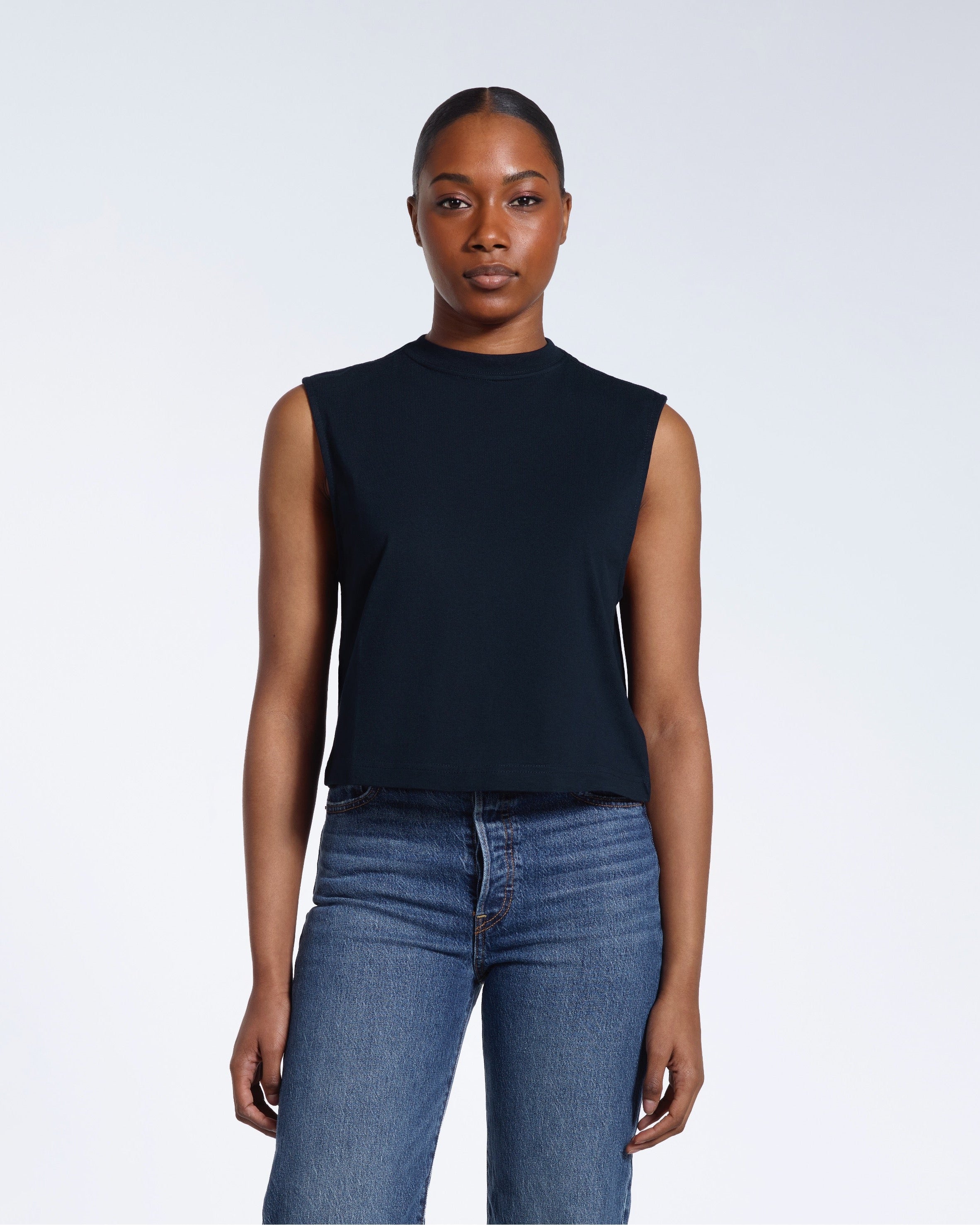 A woman facing front on looking at the camera, modelling a navy sleeveless organic cotton tank top.