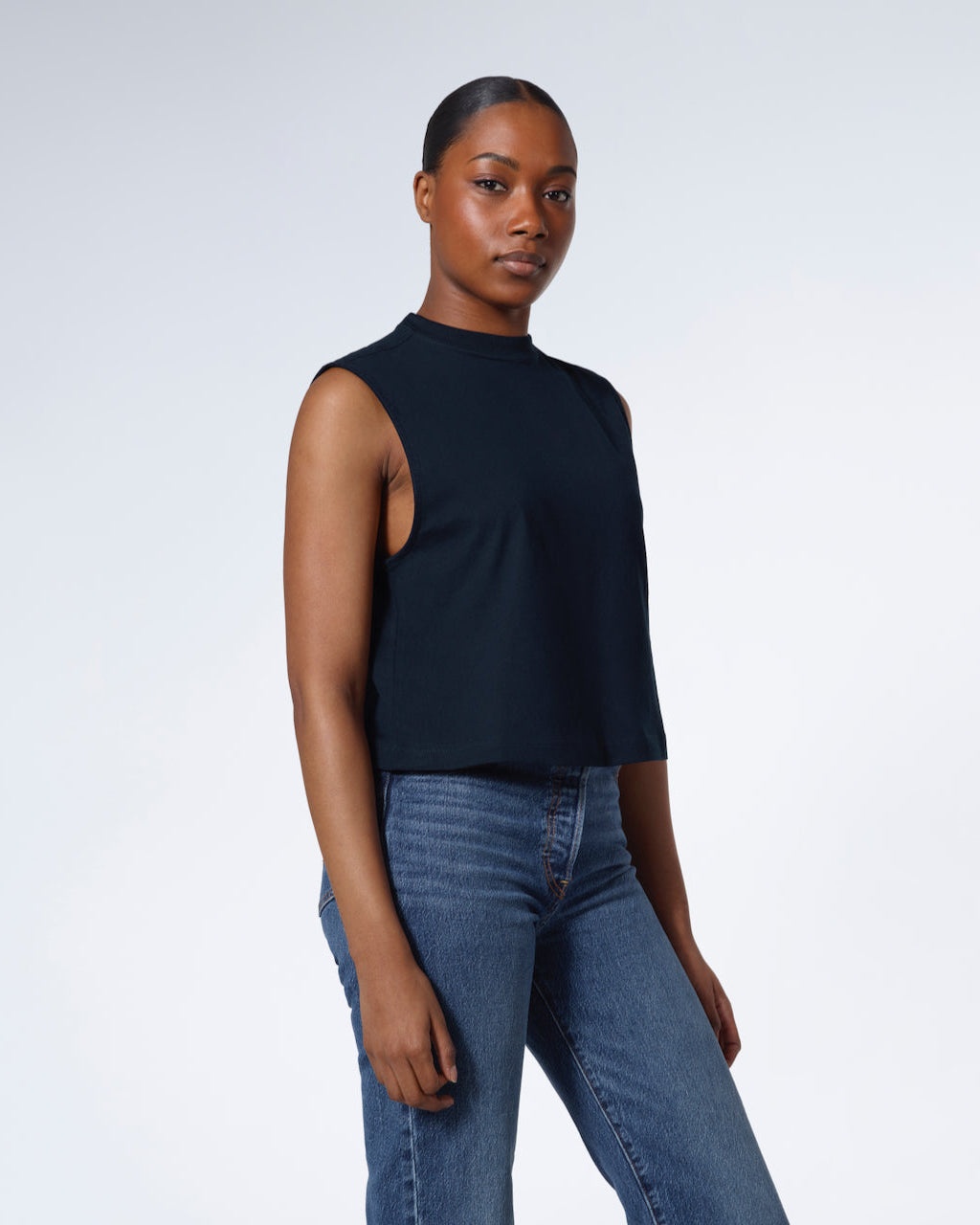 A woman looking into the camera with her hands by her sides, modelling a plain navy sleeveless organic cotton tank top.
