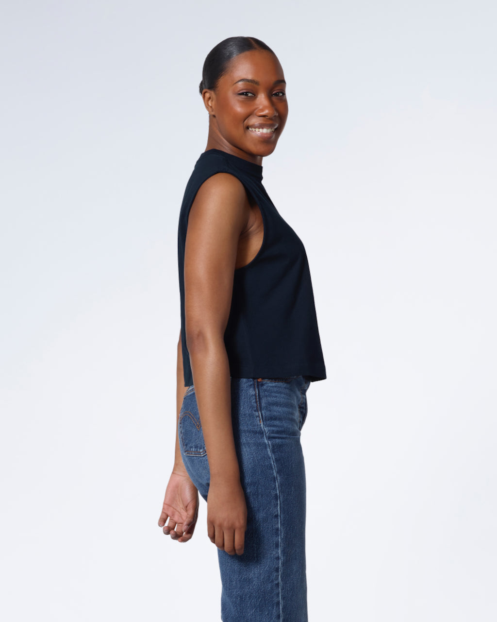 A woman facing side on and looking at the camera, modelling a plain navy sleeveless organic cotton tank top.