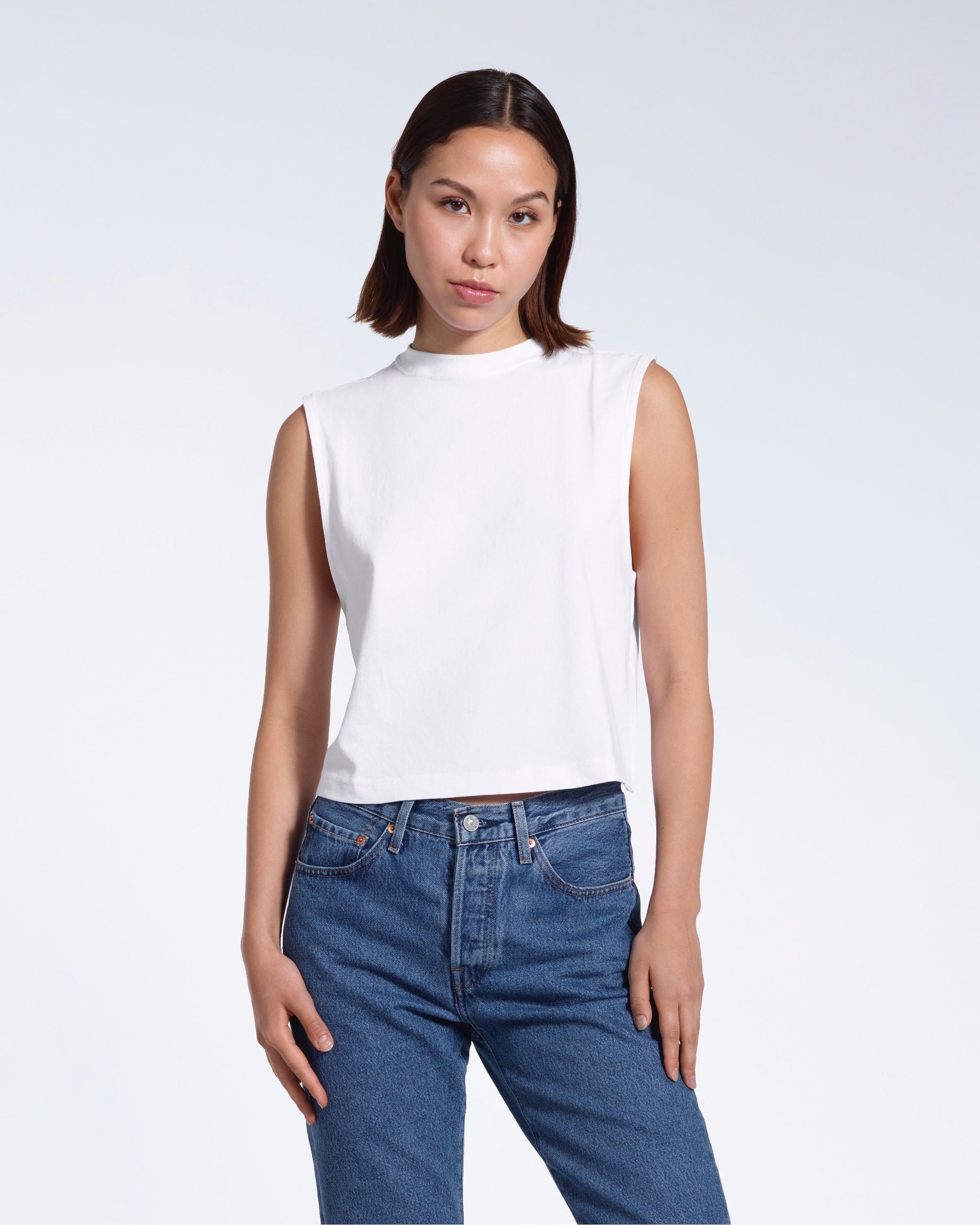 A woman facing front on looking at the camera, modelling a white short sleeve organic cotton tank top.