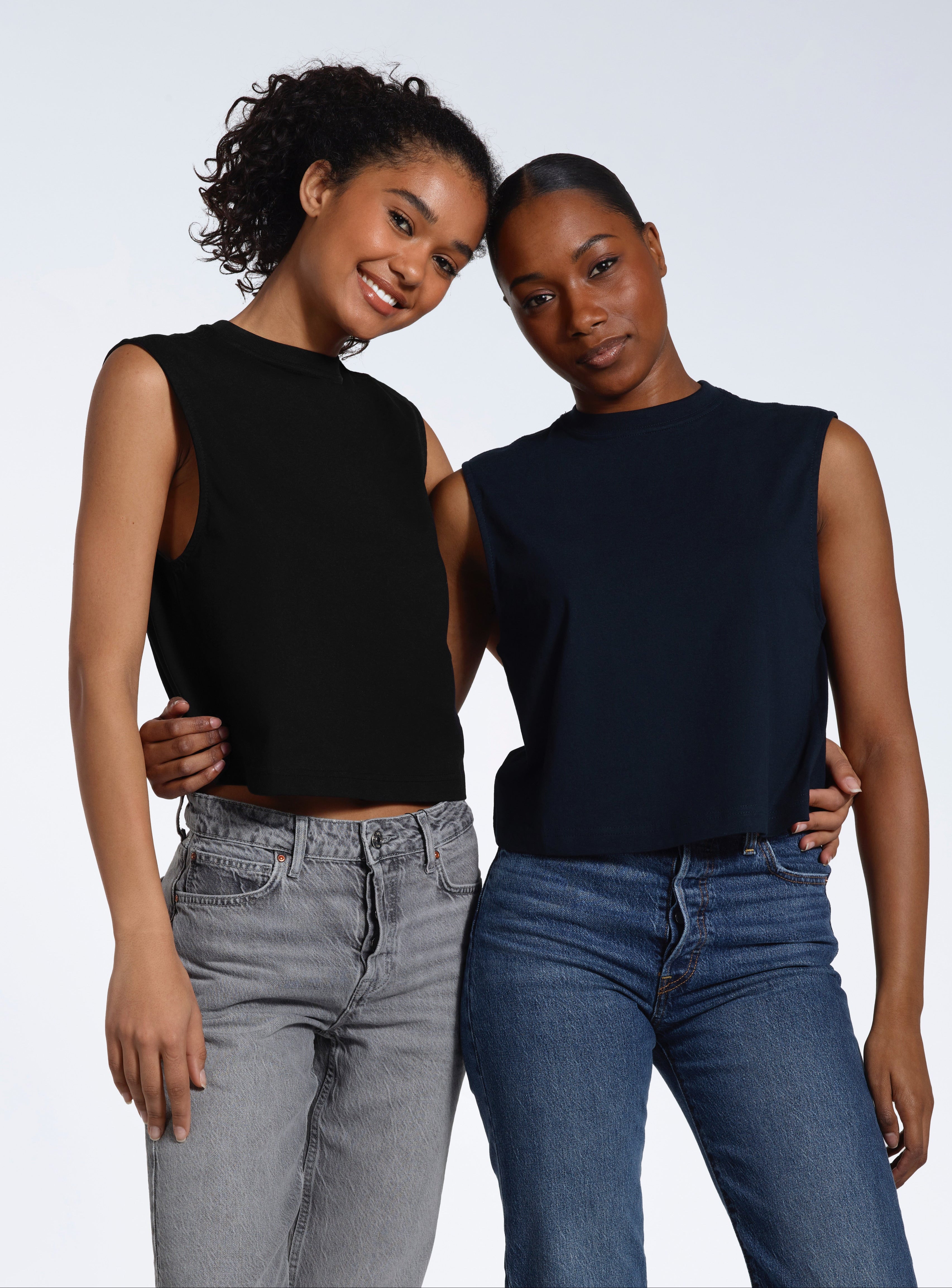 Two women with their arms around eachother smiling into the camera, modelling plain black and navy organic cotton tank tops.