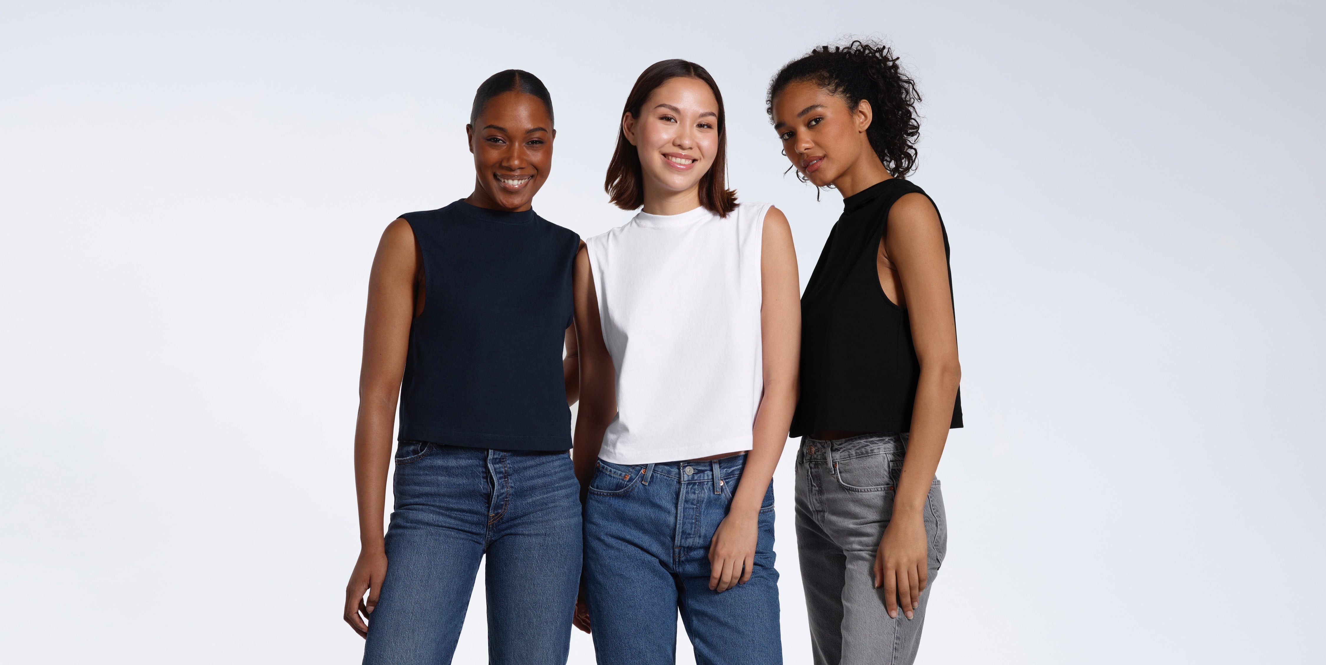 Three women looking into the camera, modelling plain black, white and navy organic cotton tank tops.