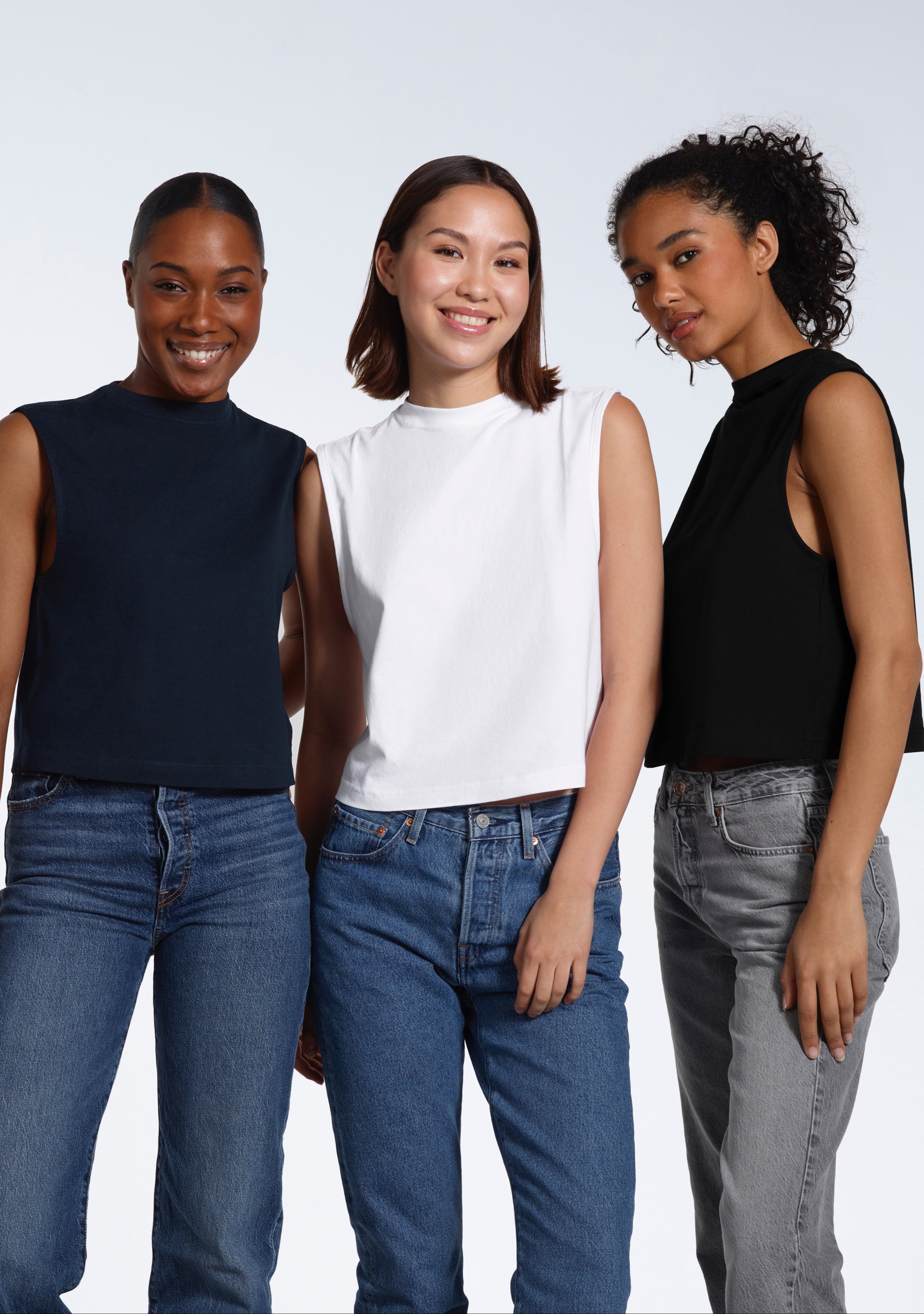 Three women looking into the camera, modelling plain black, white and navy organic cotton tank tops.