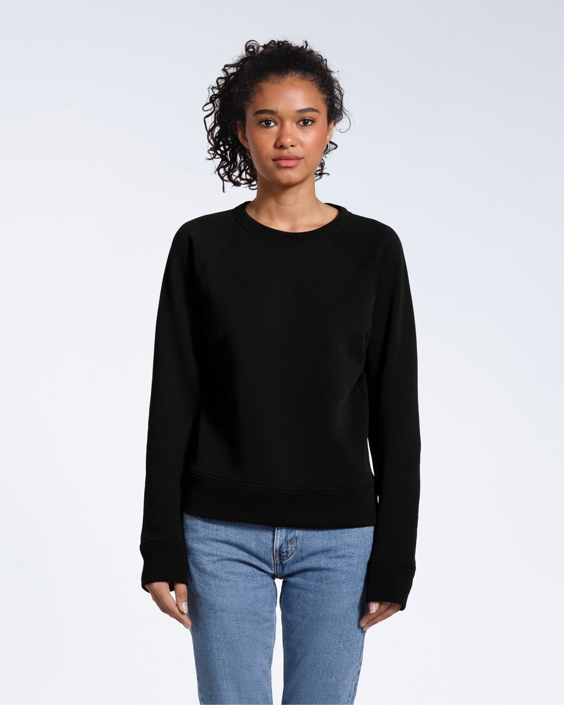 A woman face on looking into the camera with her arms by her side, modelling a plain black french terry organic cotton sweatshirt.