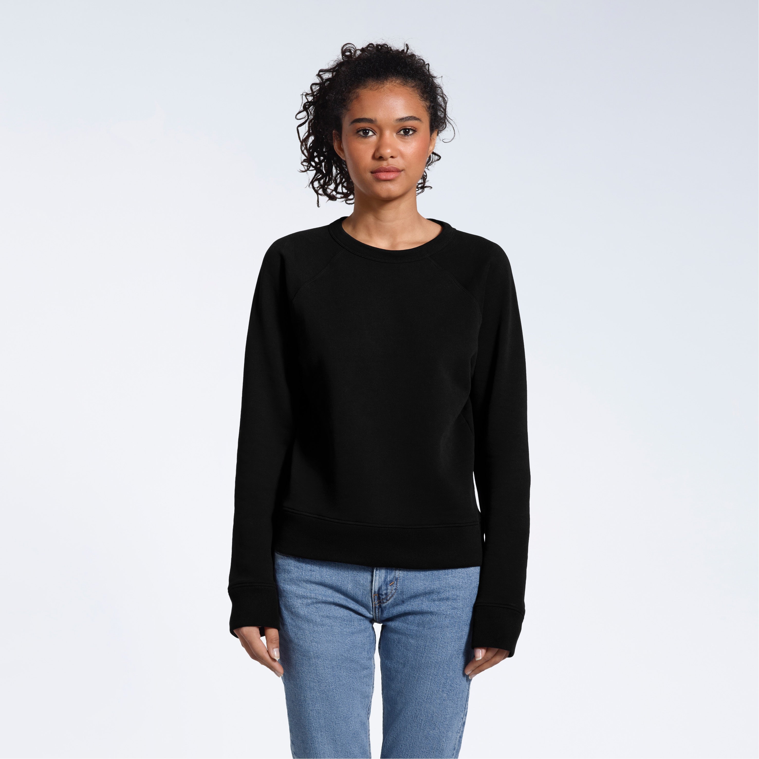 A woman face on looking into the camera with her arms by her side, modelling a plain black french terry organic cotton sweatshirt.